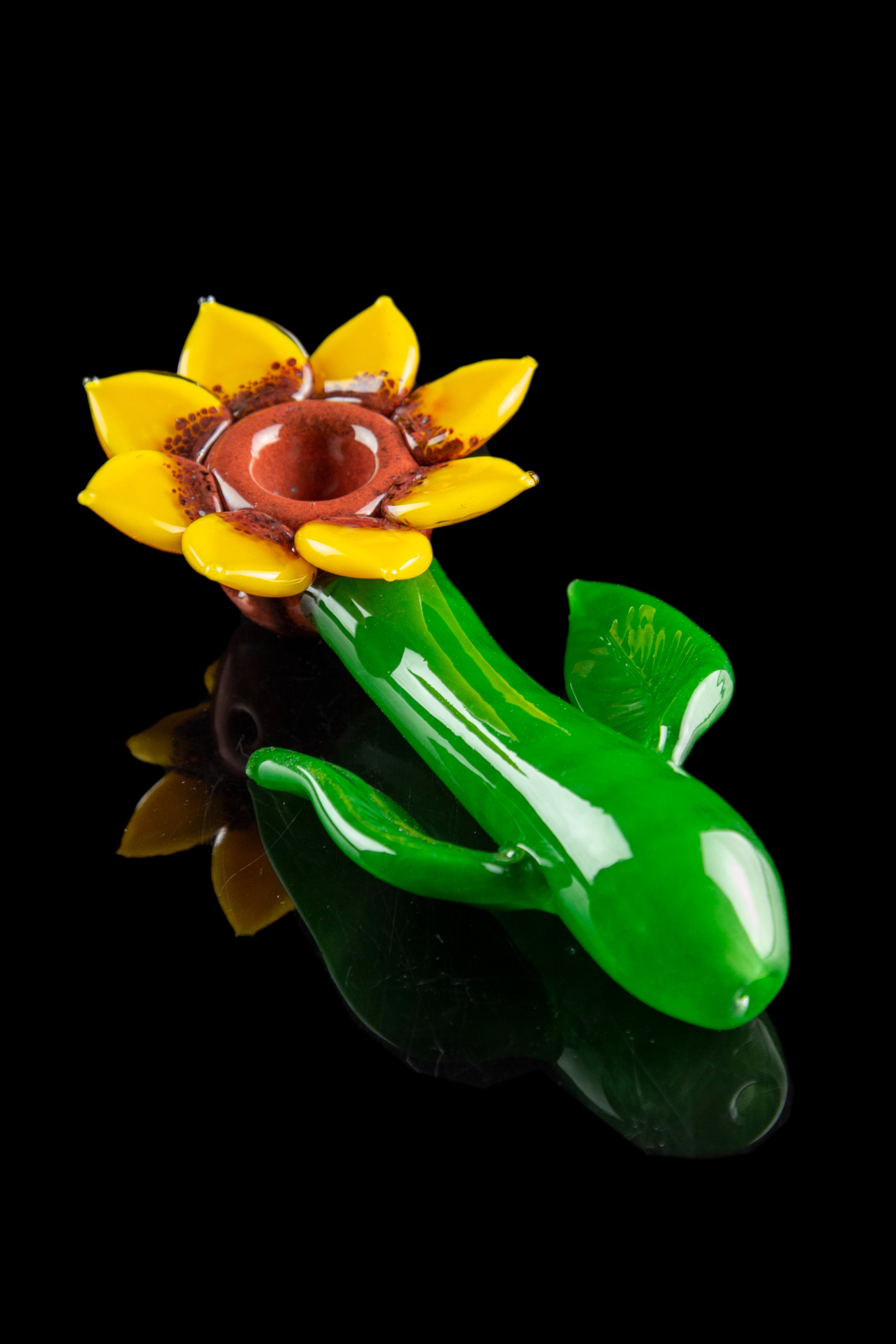 Hand-blown glass pipe shaped like a blooming flower with green stem and leaves, isolated on a black background.