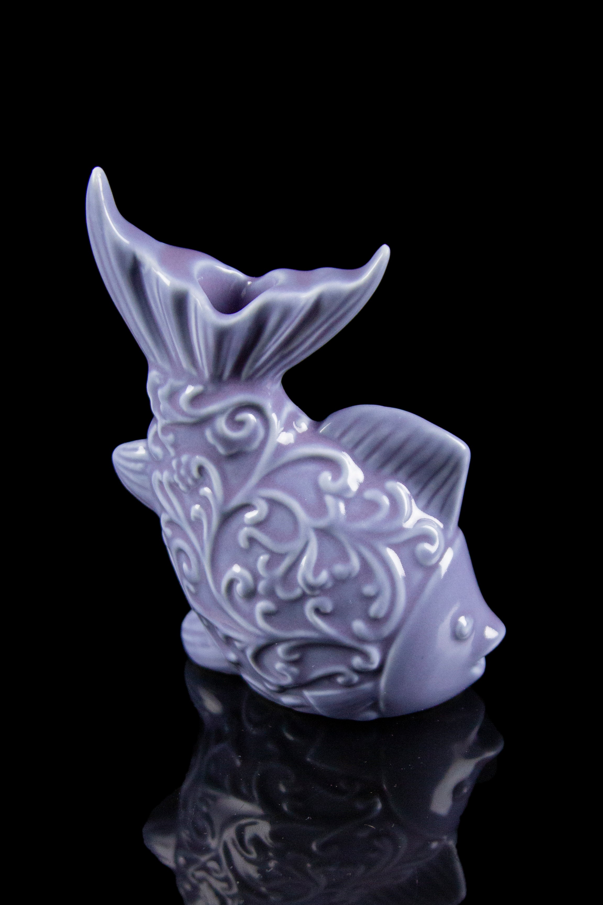 Purple ceramic fish-shaped water pipe with ornate detailing, reflecting on a glossy black surface.