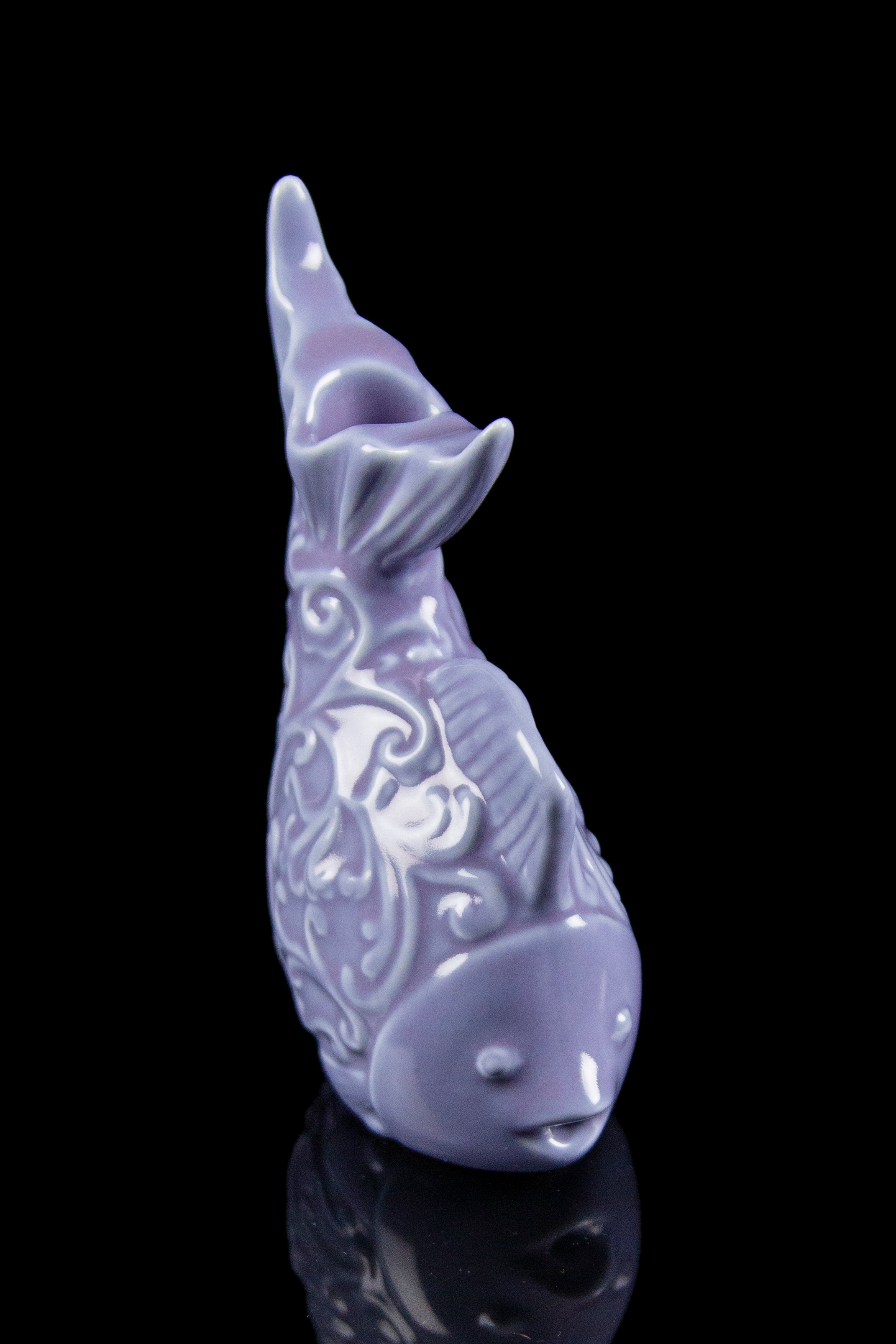 Lavender ceramic whale-shaped water pipe with ornate detailing, reflecting on a dark surface.