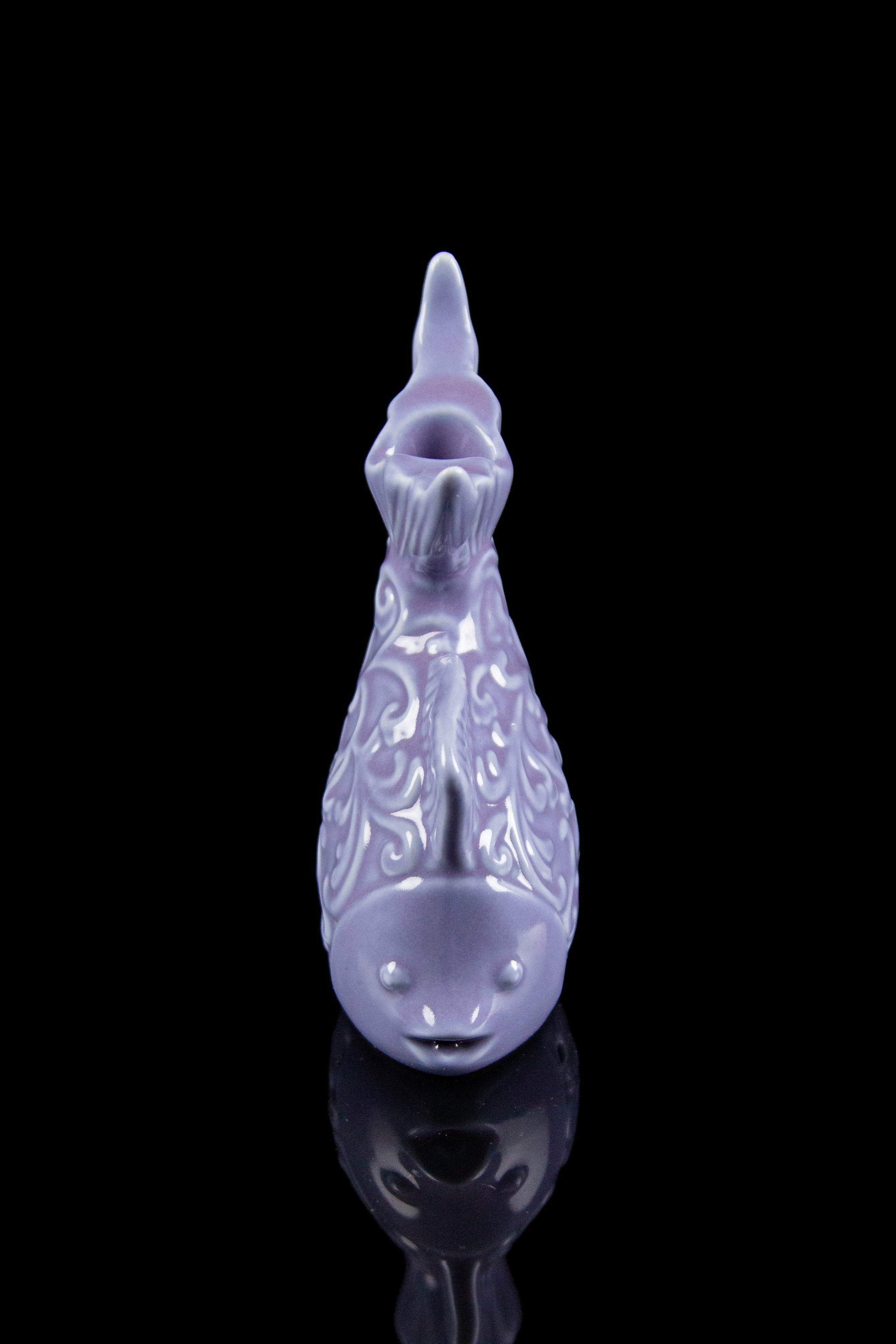 Lavender glass cannabis water pipe with ornate carving, reflected on a glossy black surface.