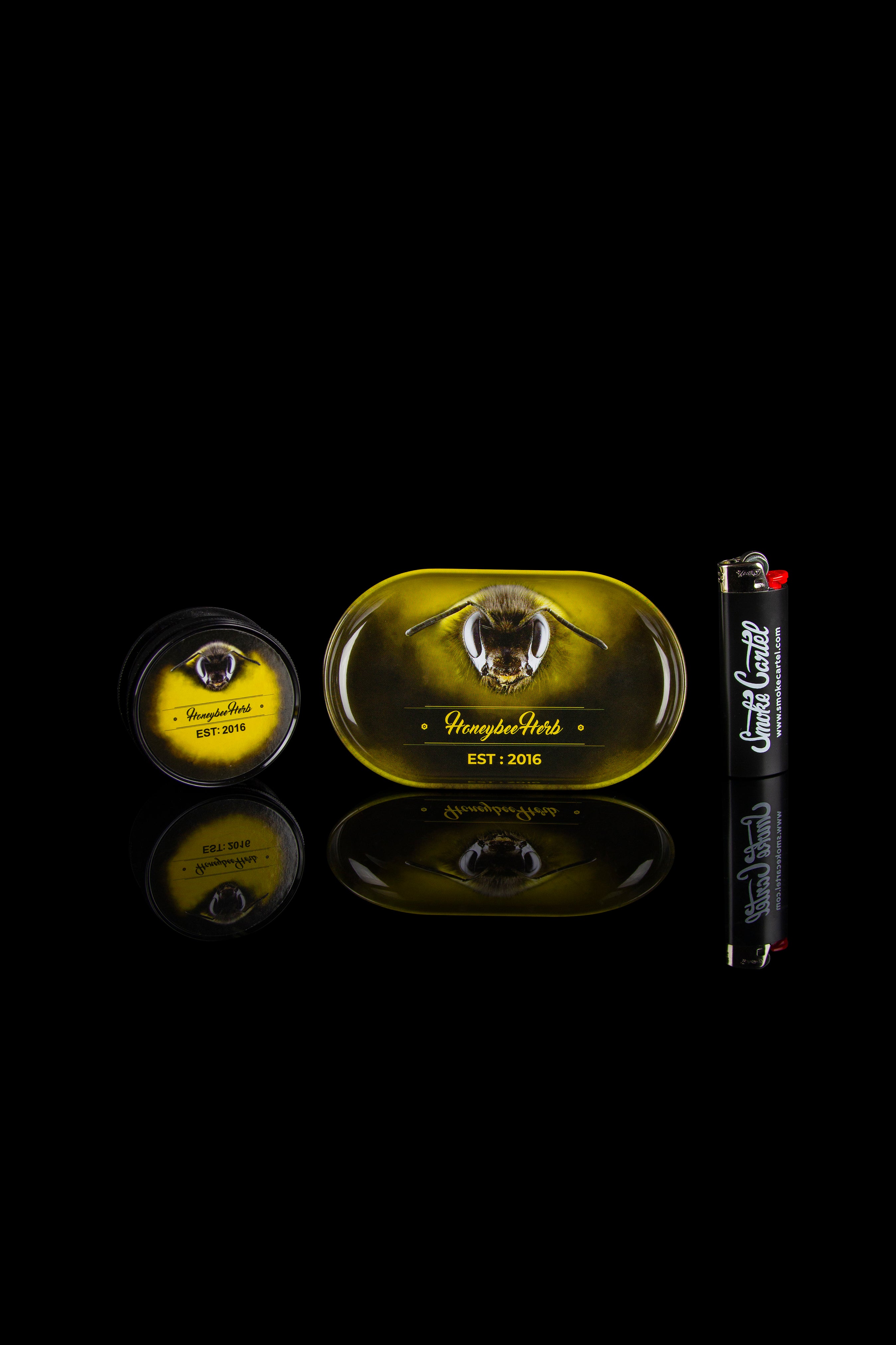 Product shot of Honeybee Herbs cannabis tins and rolling paper packaging on a reflective black surface.