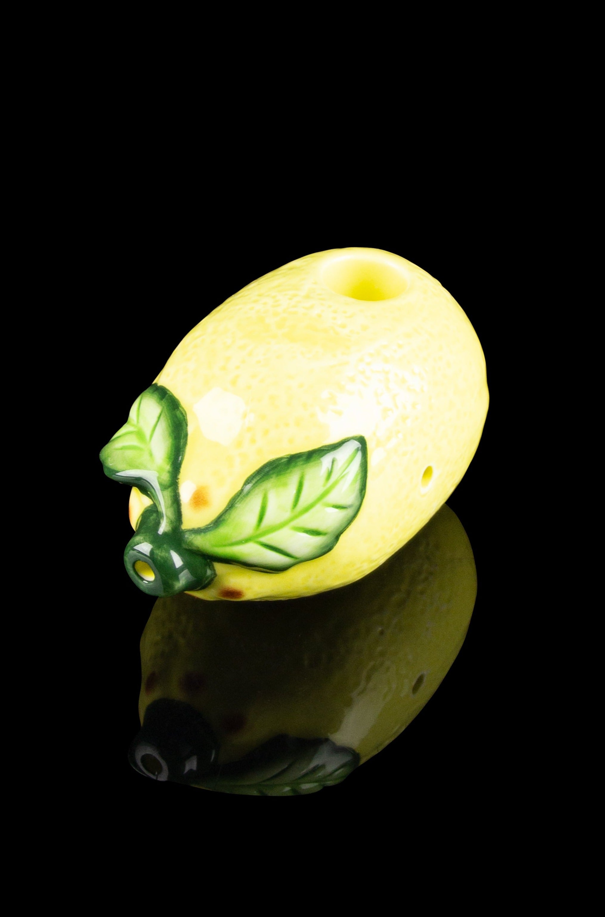 Glowing yellow cannabis oil dab rig shaped like a lemon with green leaf accents, reflected on a black surface.