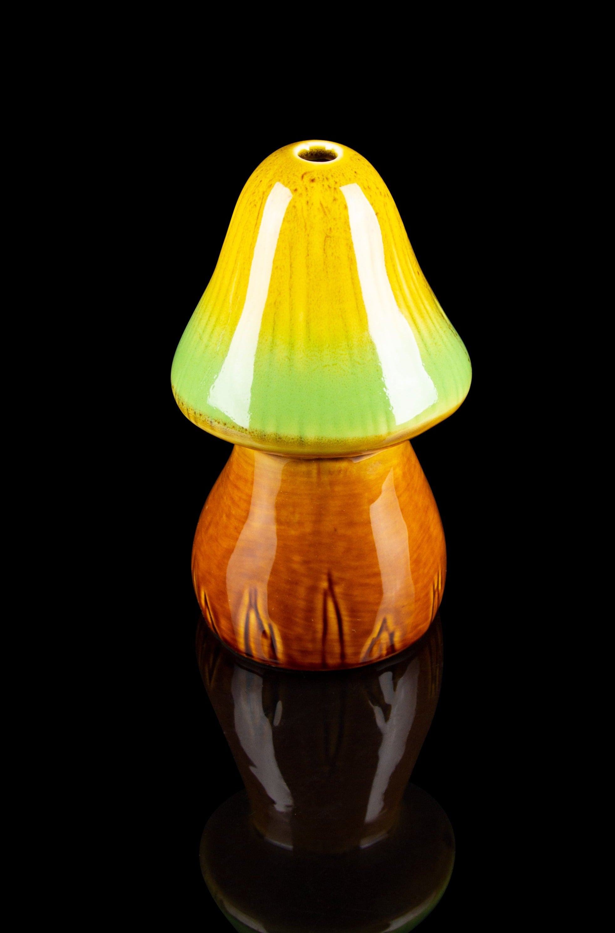 Hand-blown glass mushroom-shaped water pipe with gradient orange and green coloring, isolated on black.