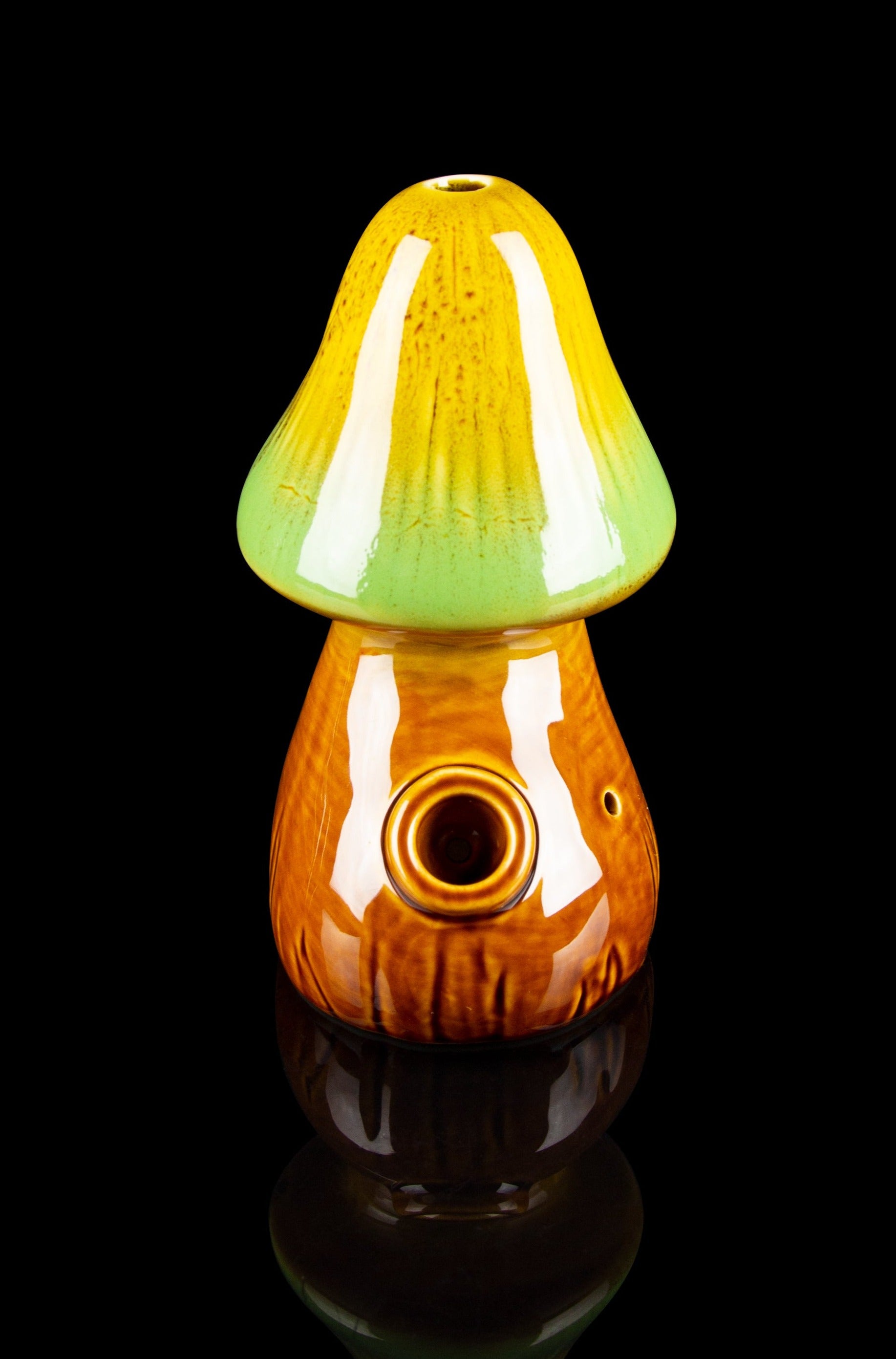 Glass mushroom-shaped pipe with orange and green swirls, reflecting on a black surface.