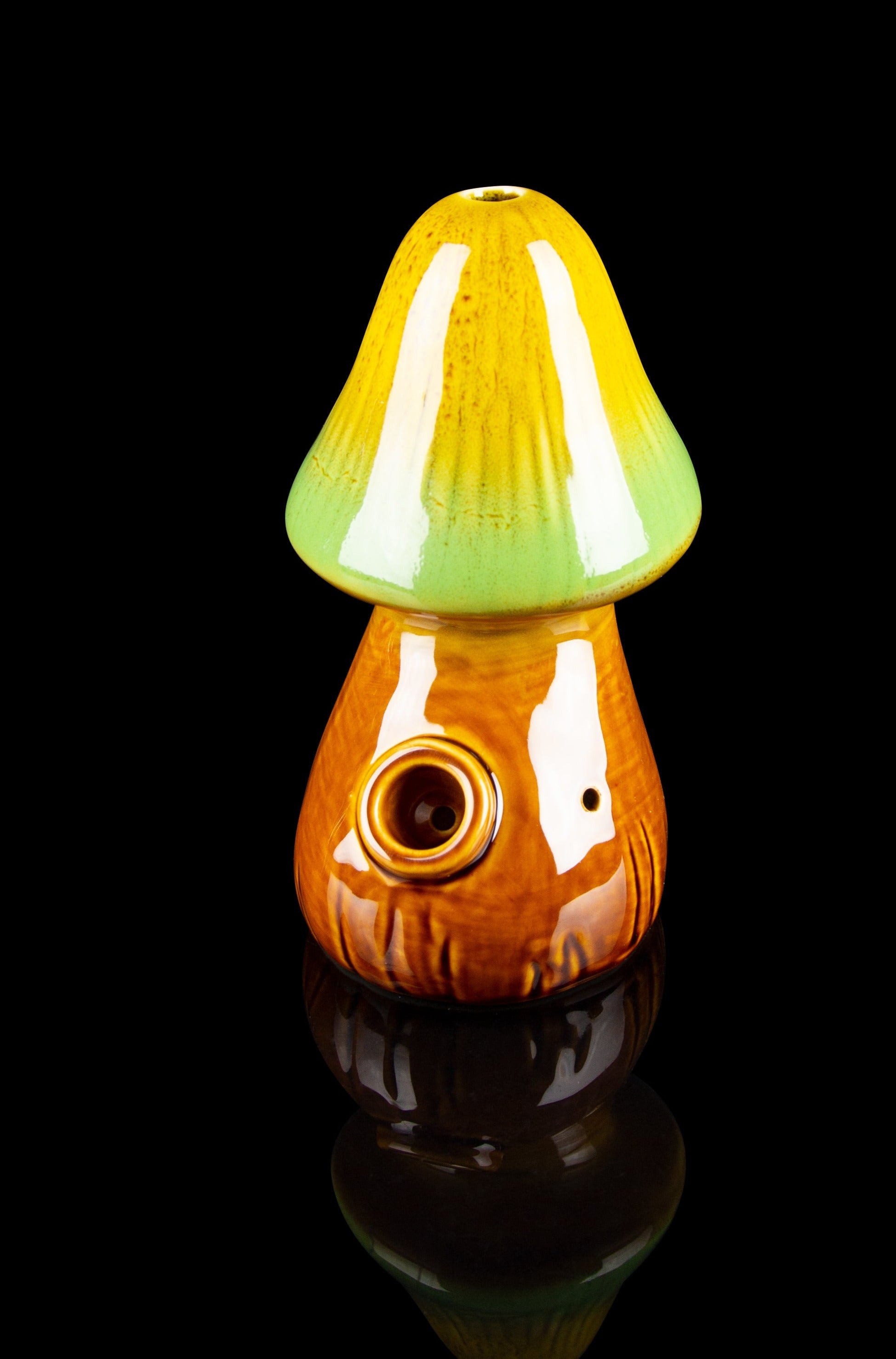 Glass mushroom-shaped water pipe with orange and green coloring, reflected on a dark surface.