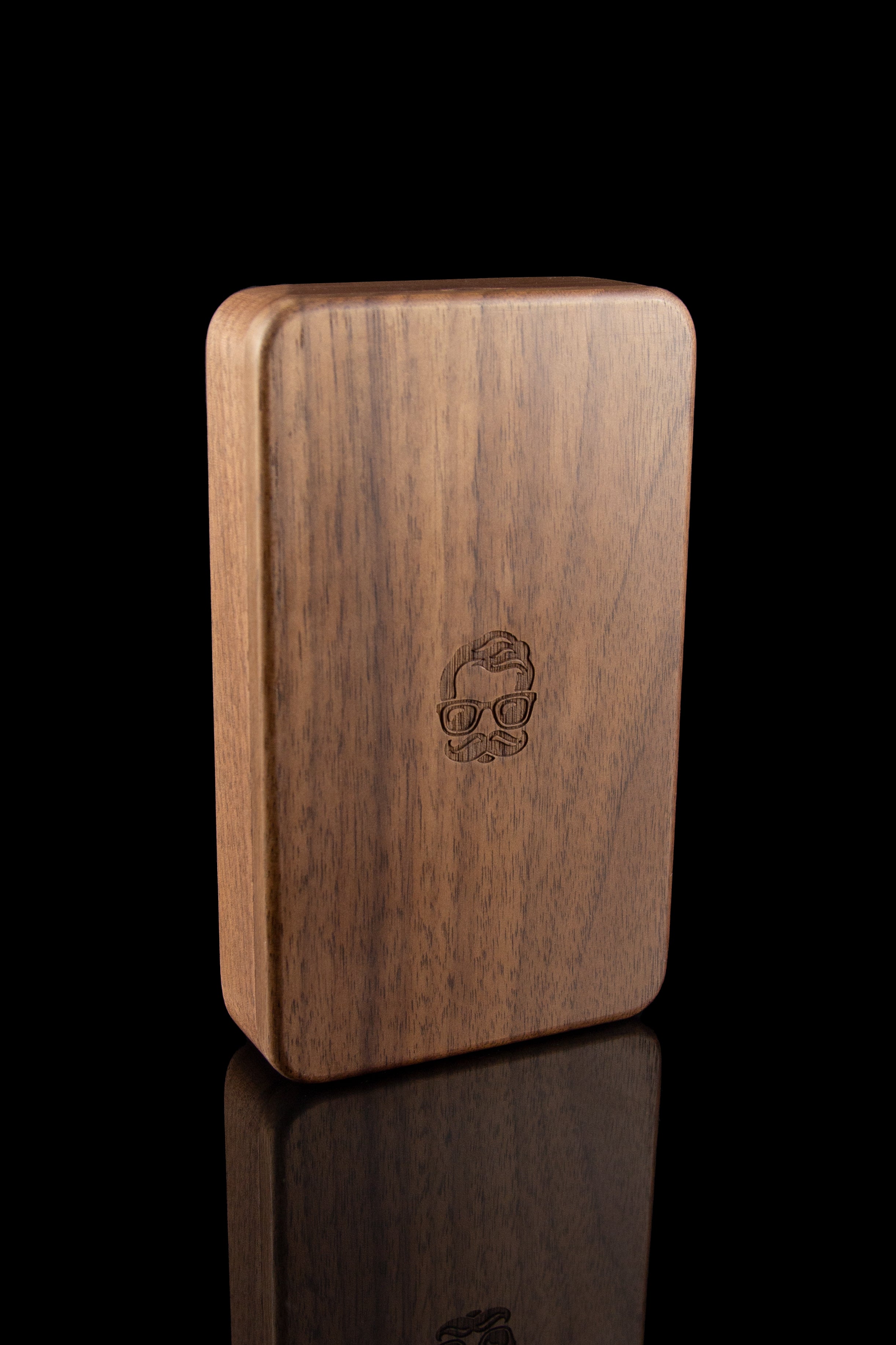 Wooden cannabis storage box with engraved skull design, displayed on a reflective surface.