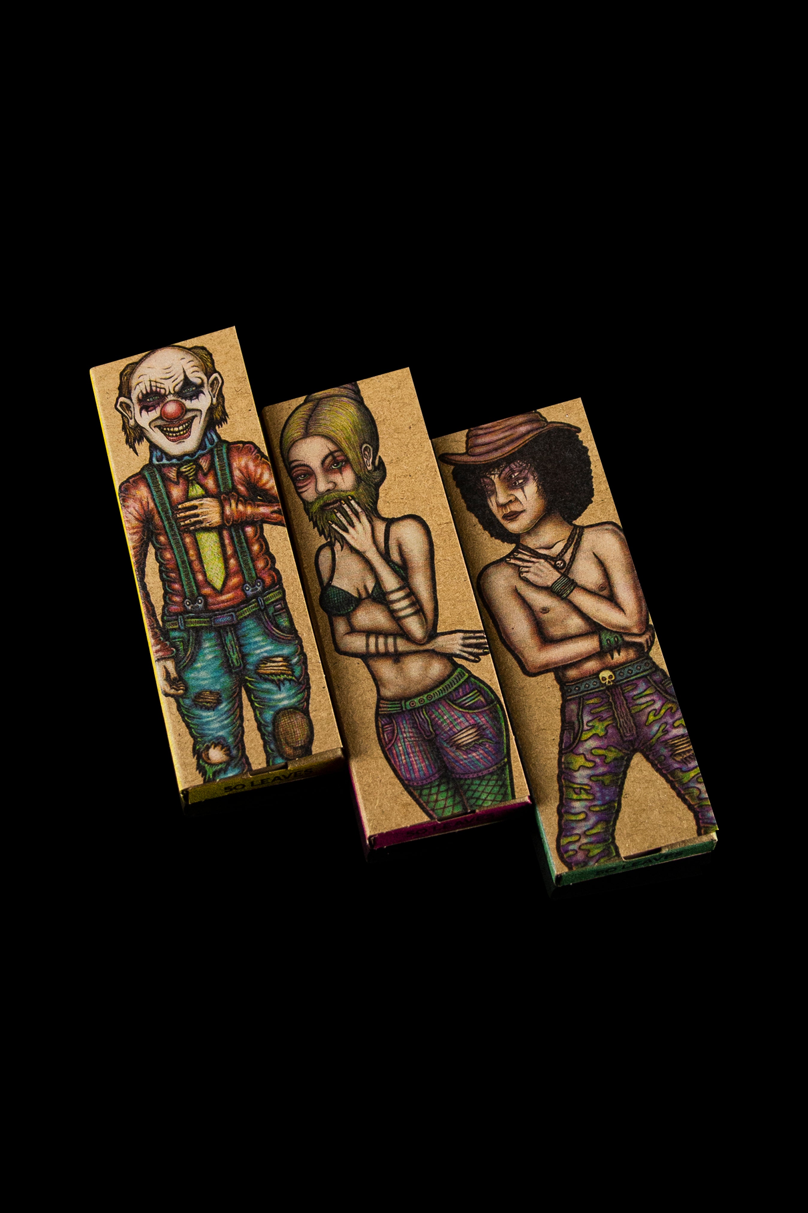 Three uniquely illustrated rolling paper booklets with darkly whimsical character designs against a black background.