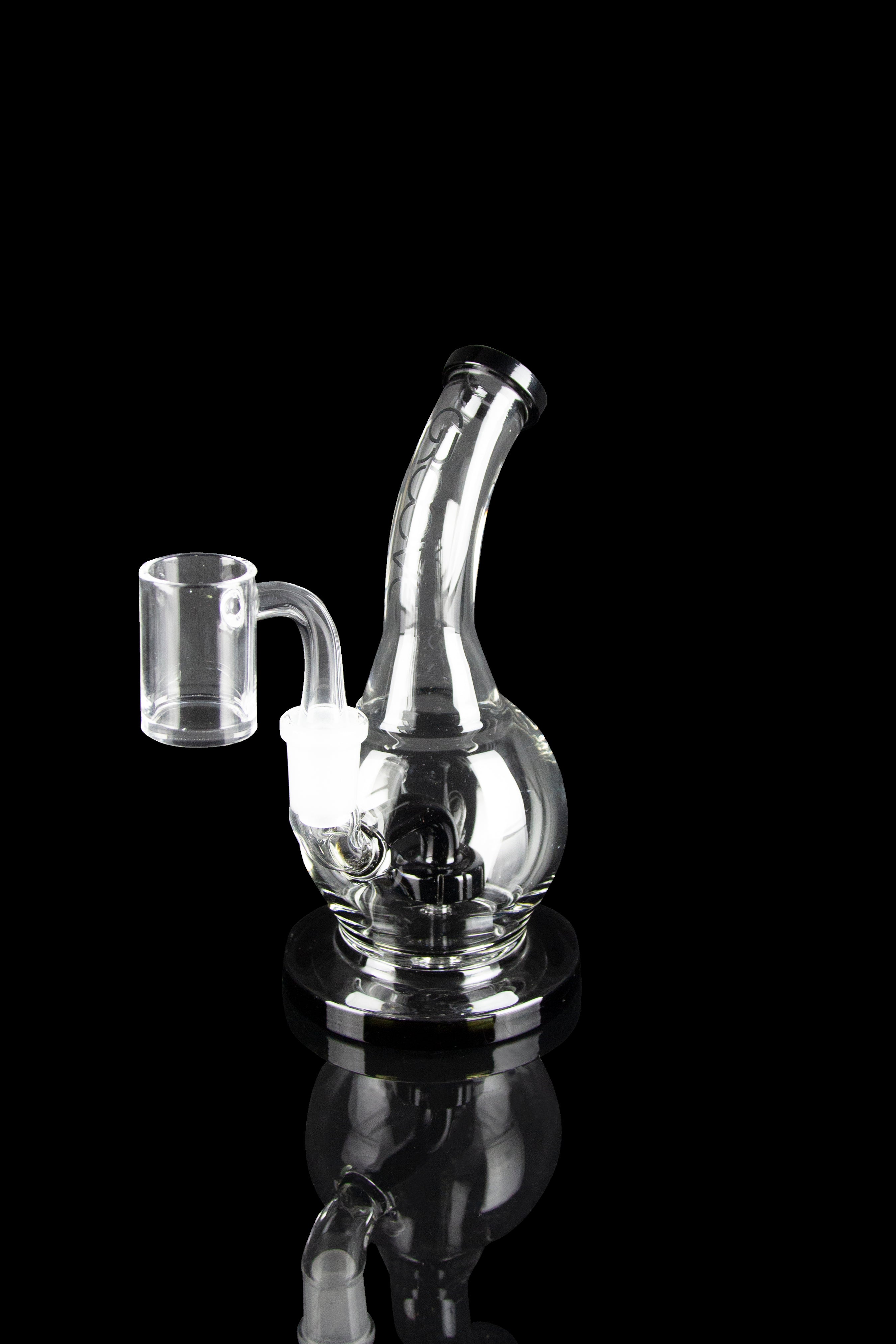 Clear glass dab rig with a quartz banger, reflecting on a black surface.
