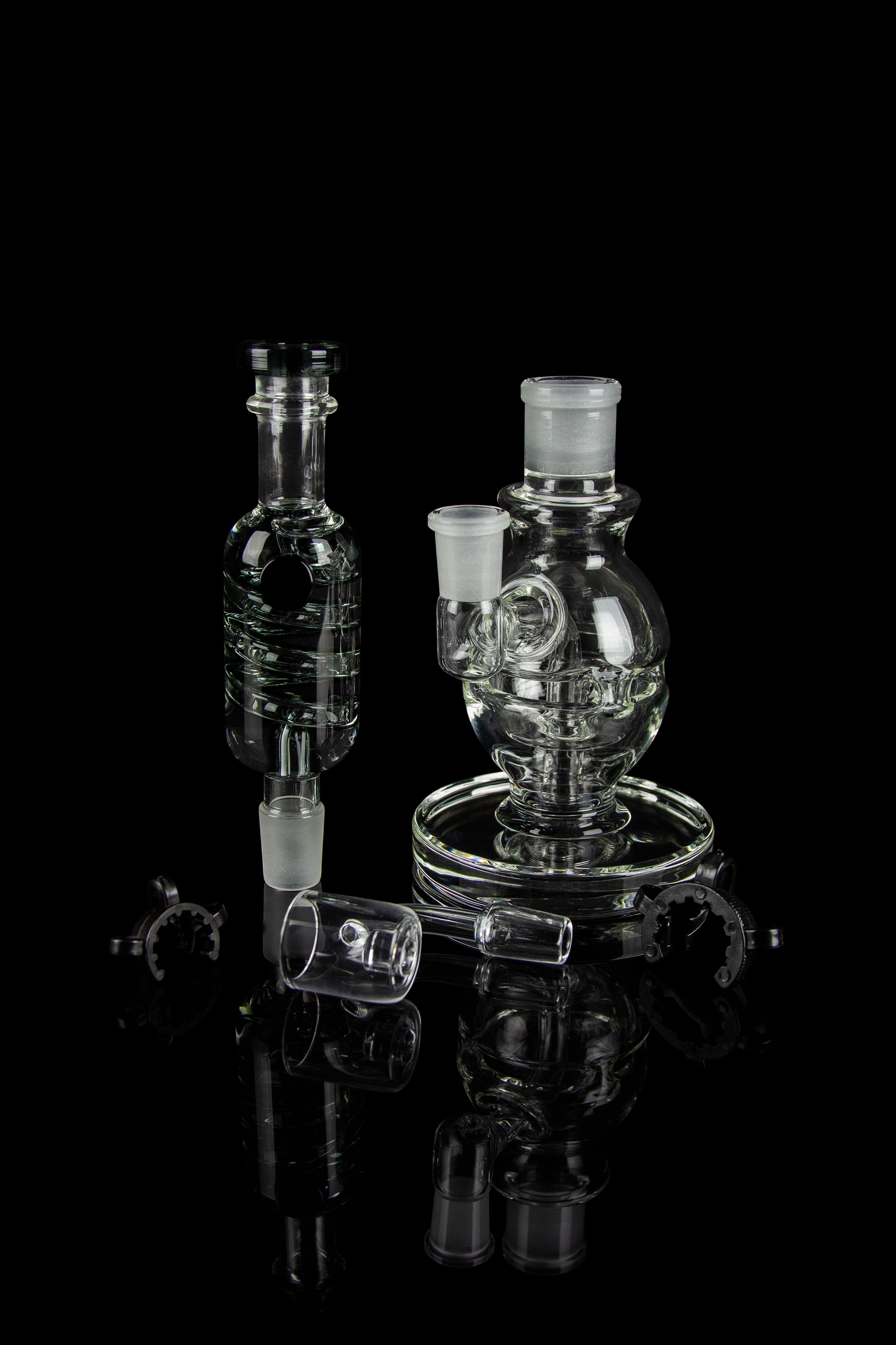 Clear glass dab rigs and accessories displayed on a reflective black surface.