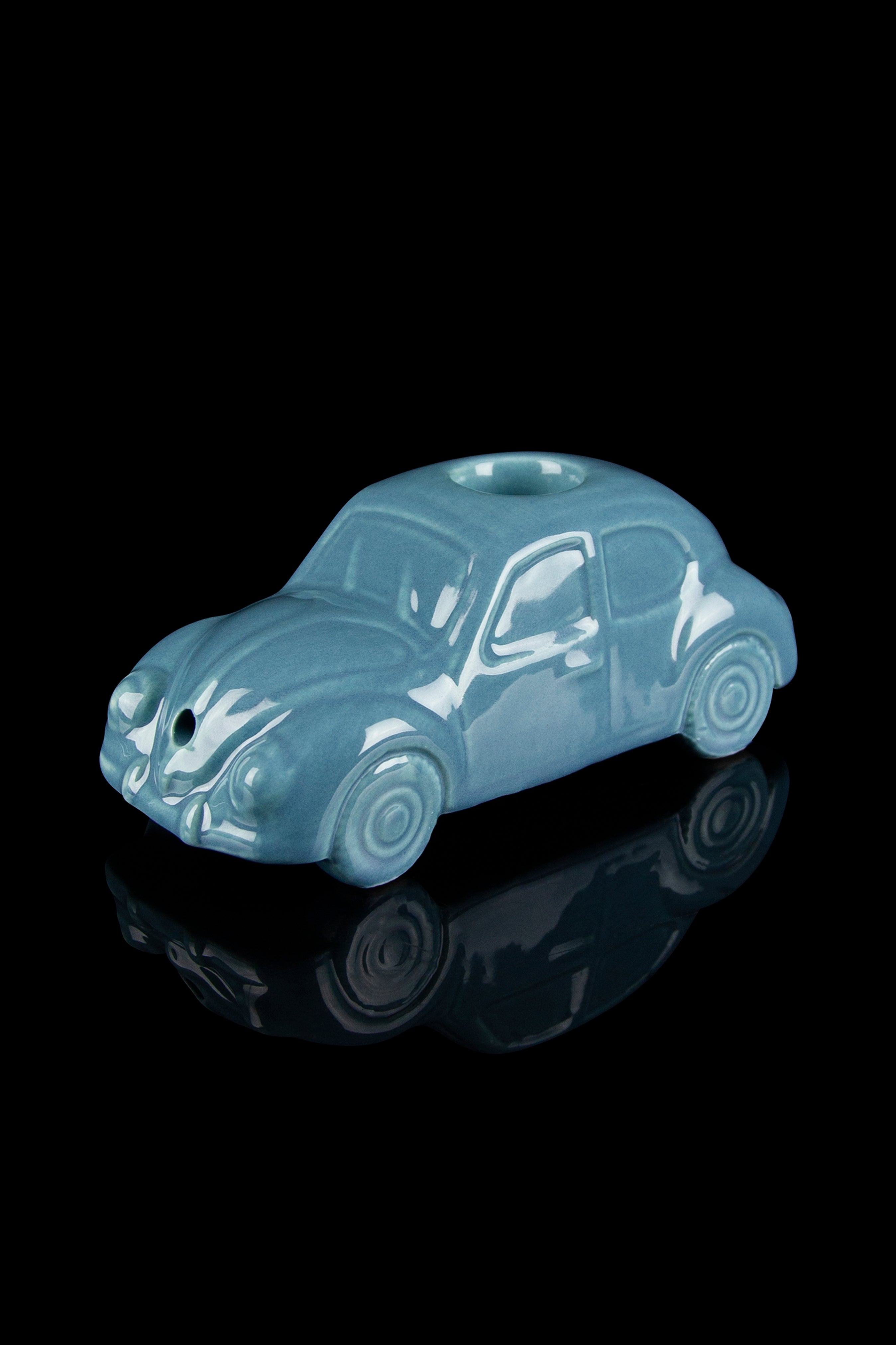 Ceramic Volkswagen-shaped pipe with a glossy teal glaze, reflecting on a black surface.