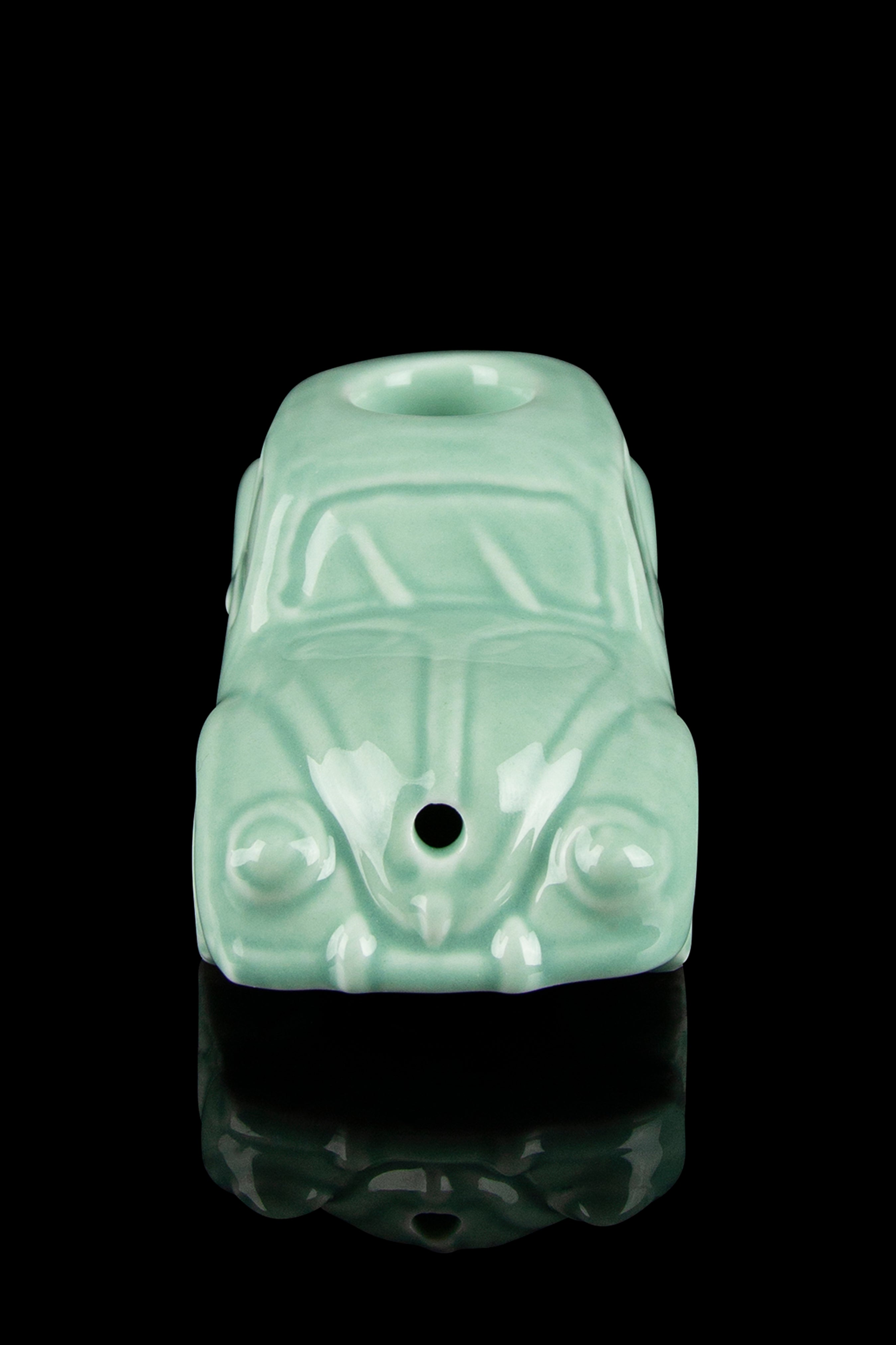 Mint green Volkswagen Beetle-shaped glass pipe with a glossy finish, reflecting on a black surface.