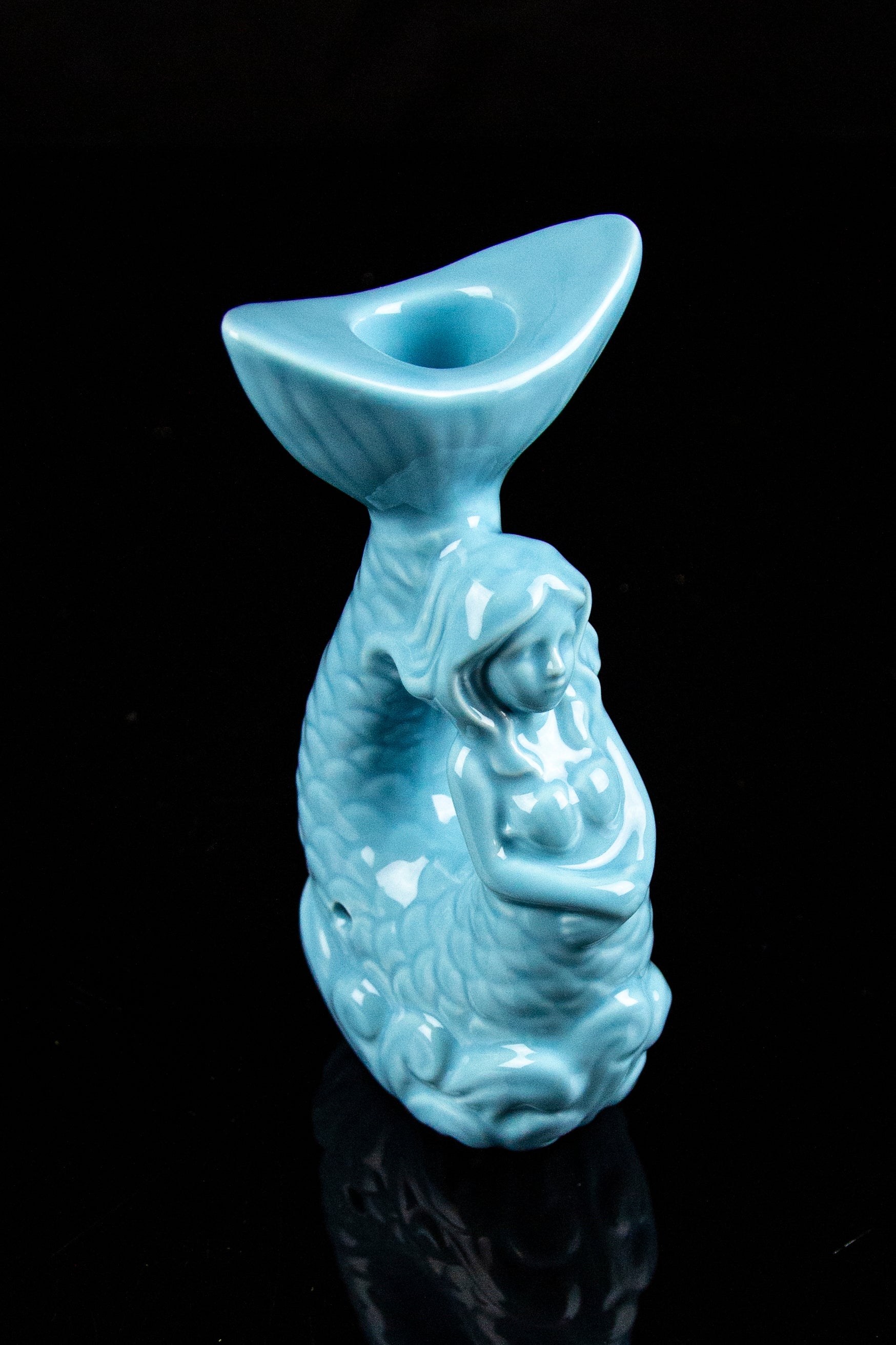 Ceramic pipe sculpted as a mermaid, turquoise glaze, against a black background.