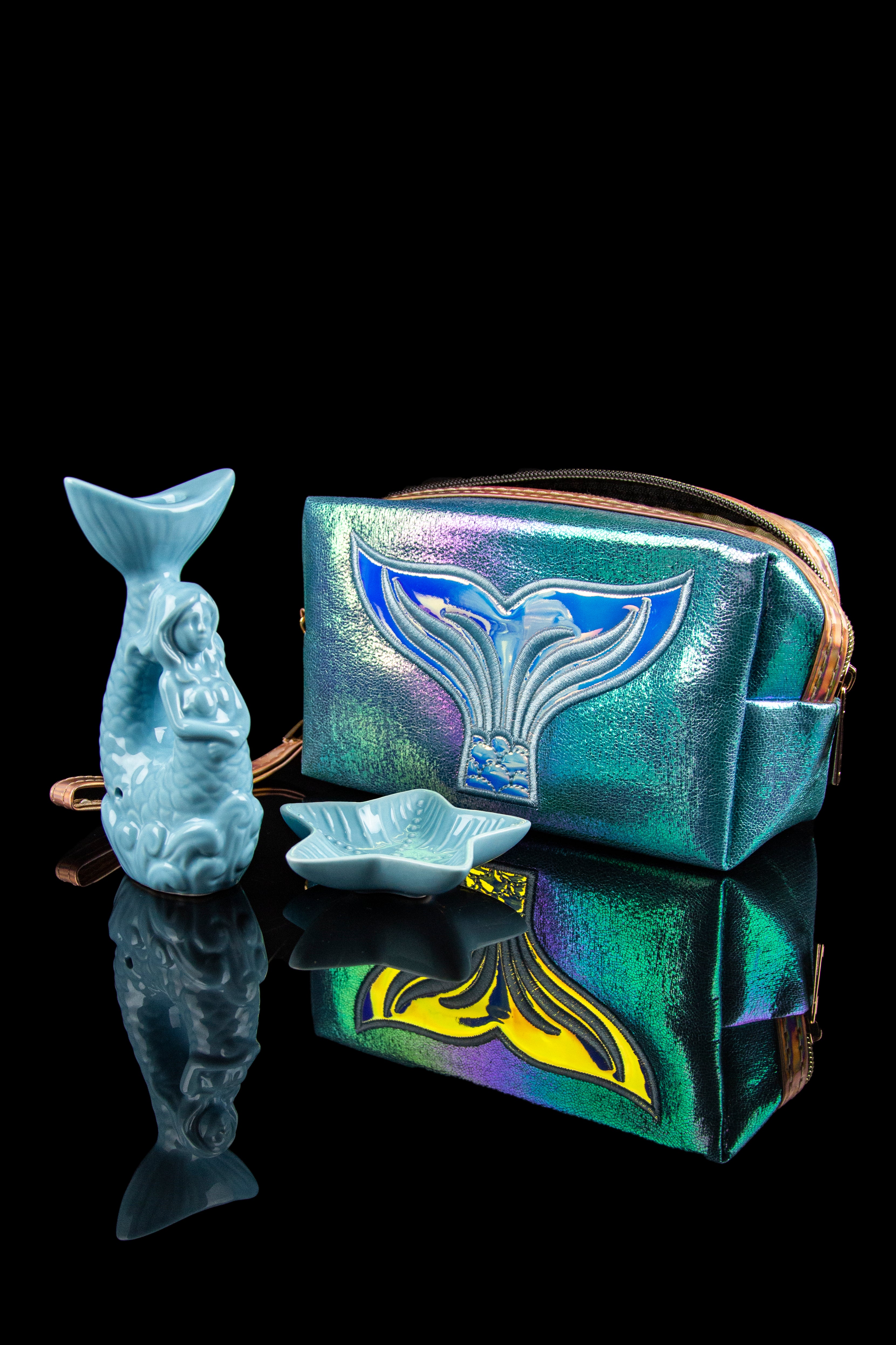 Iridescent cannabis accessory pouch with sculpted glass art depicting mythical sea creatures, reflecting on a glossy black surface.