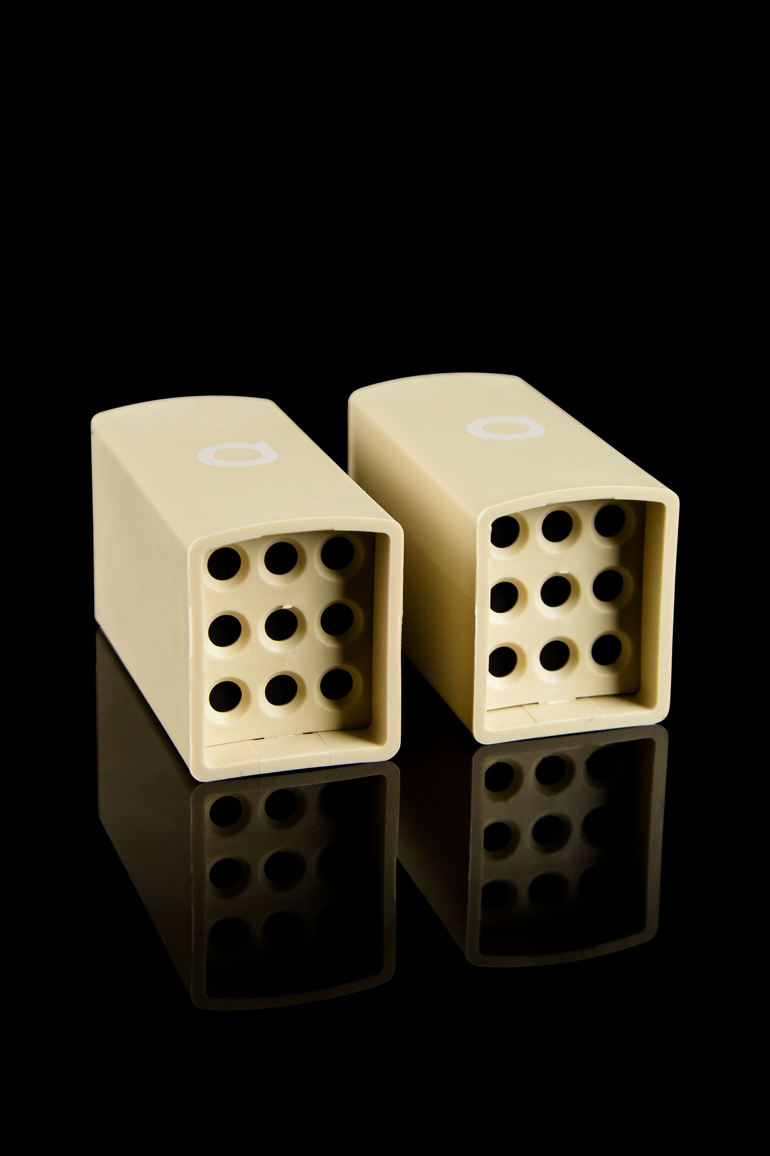 Two cream-colored one-hitters with perforated bowls rest on a reflective black surface.