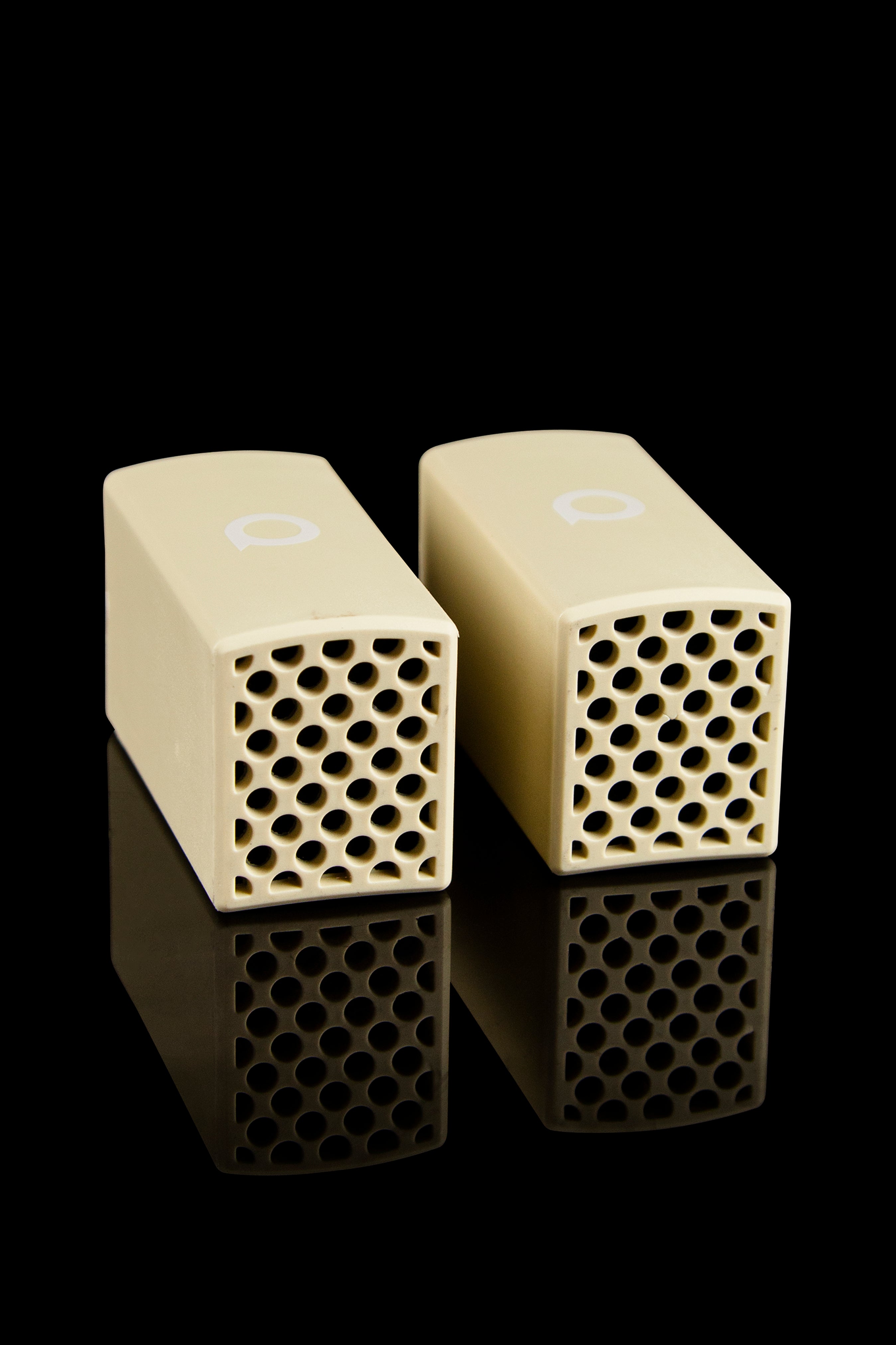 Two cream-colored ceramic cannabis filter tips with hexagonal perforations, reflecting on a black surface.