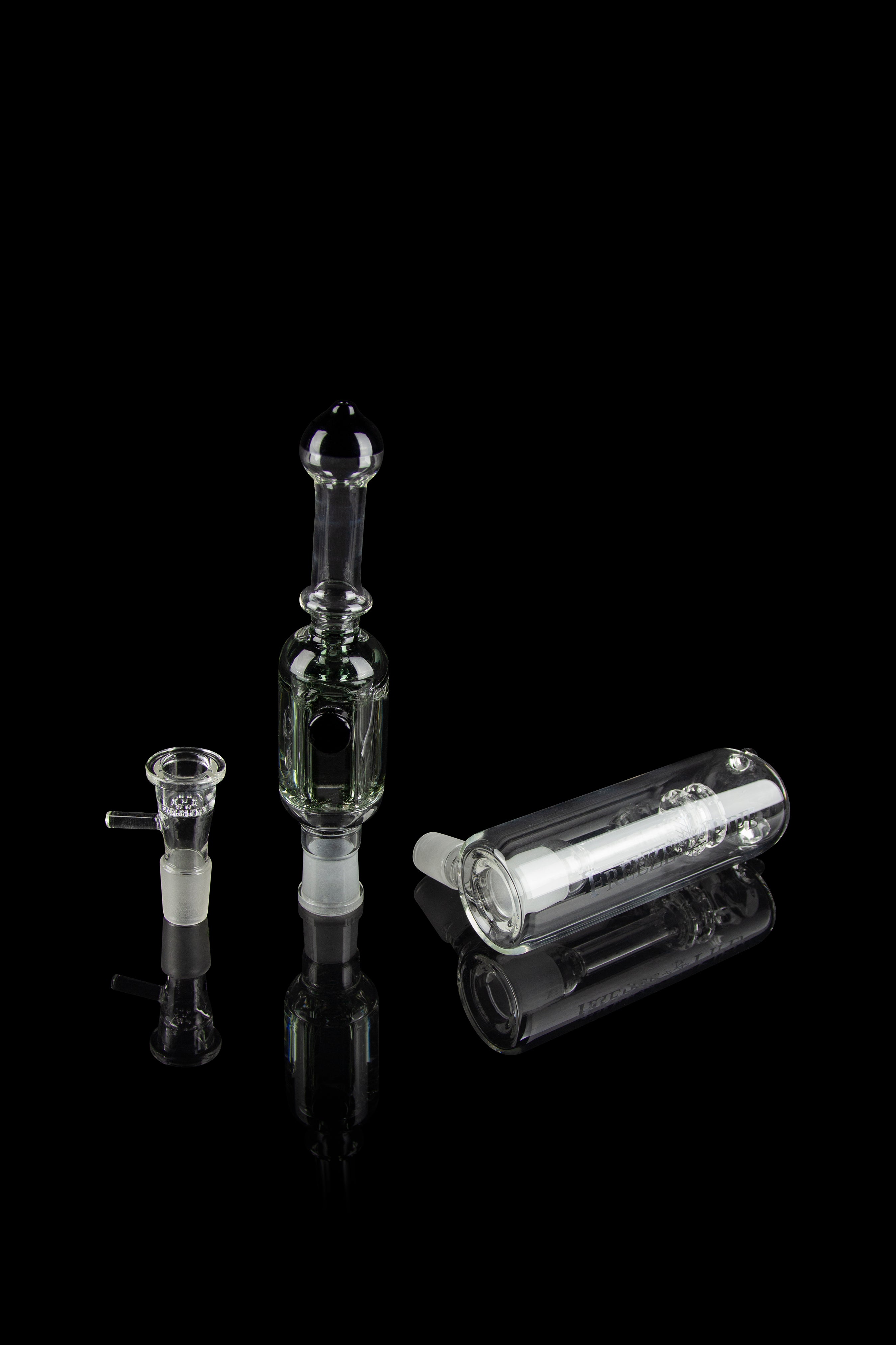 Clear glass cannabis bubbler, oil rig, and bowl displayed on a reflective surface against a black background.