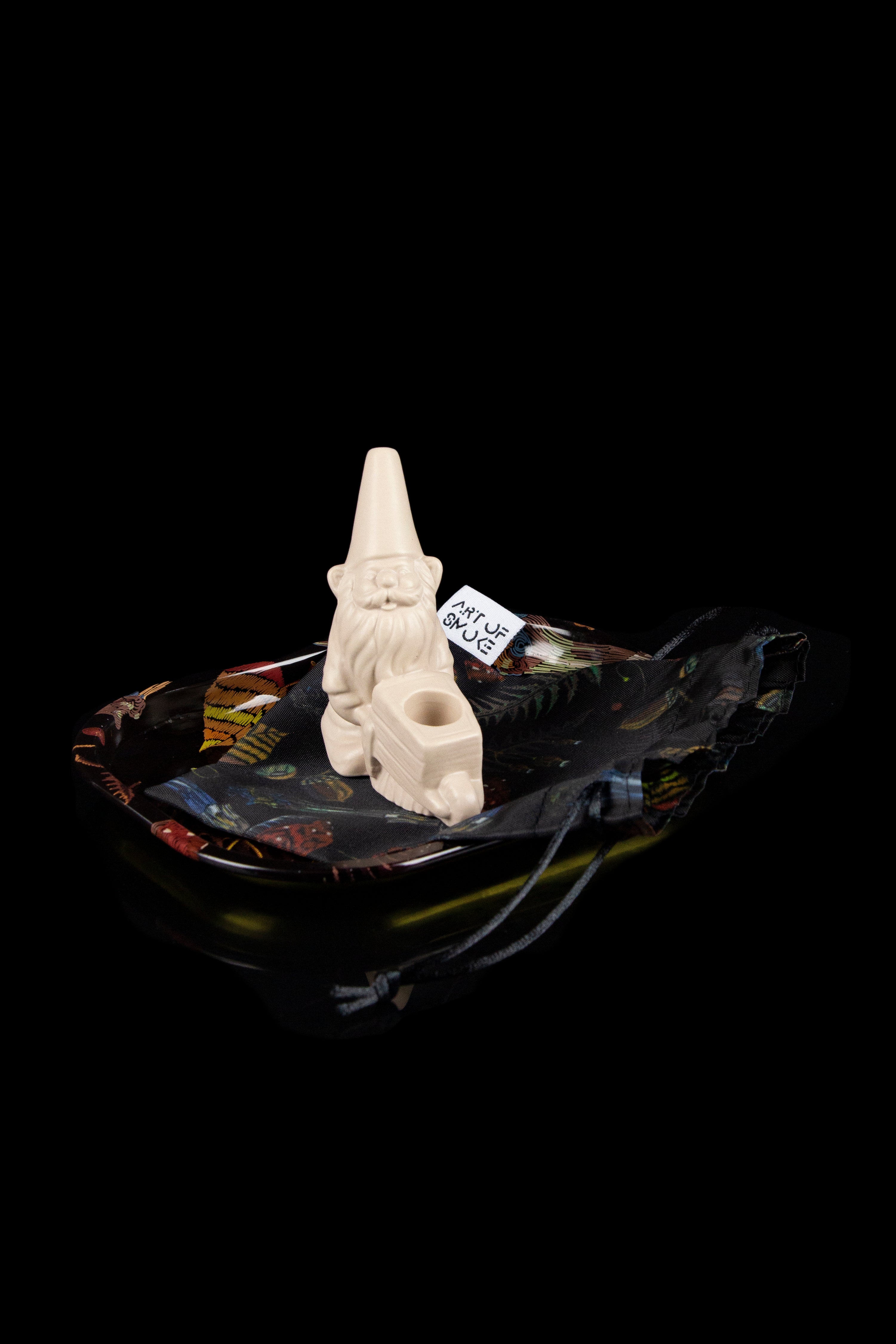 An intricately carved, bone-colored pipe rests atop a patterned ashtray against a black background.
