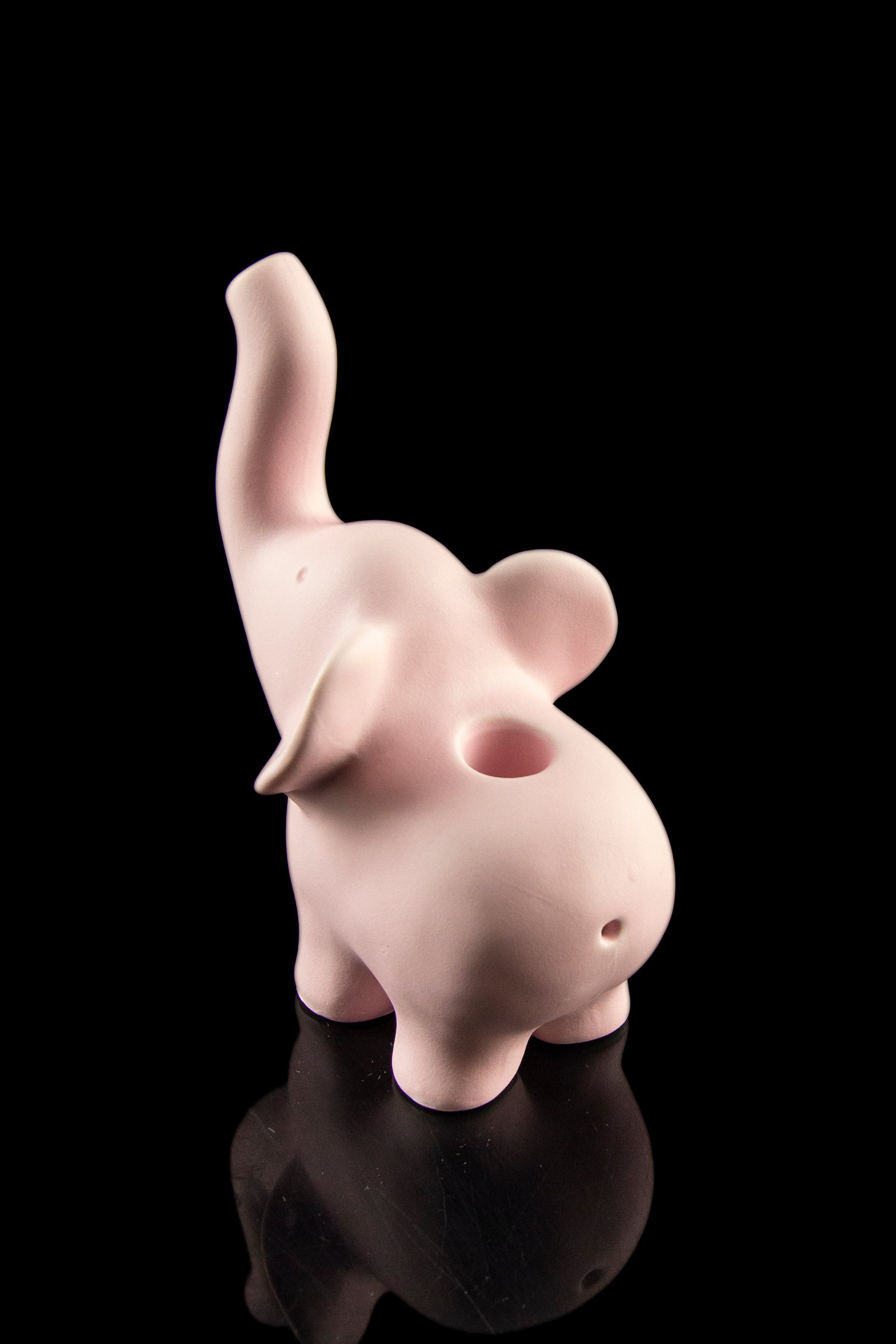 Pink ceramic elephant-shaped pipe with a glossy finish, displayed on a reflective black surface.