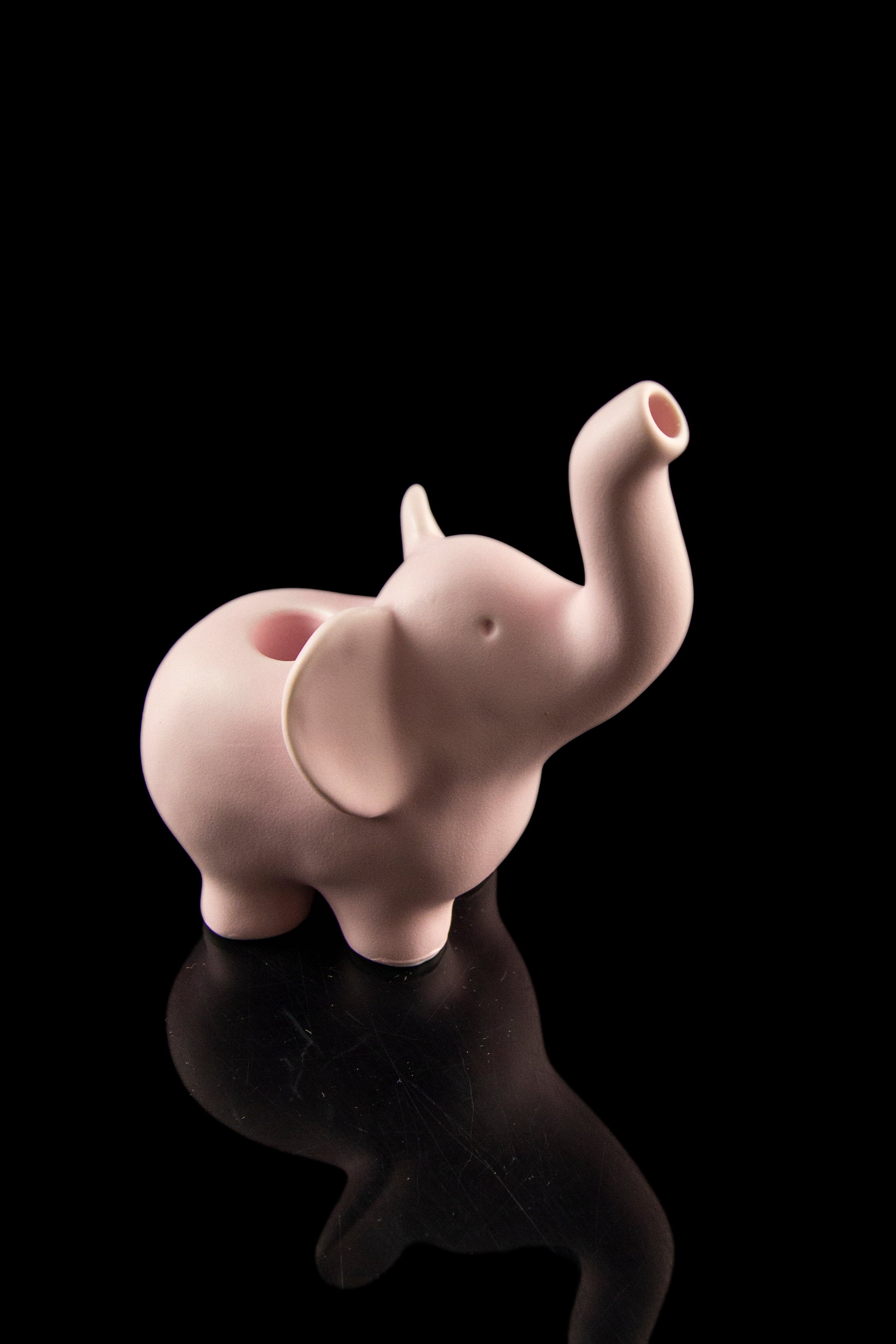 Pink ceramic elephant-shaped water pipe reflecting on a black surface.
