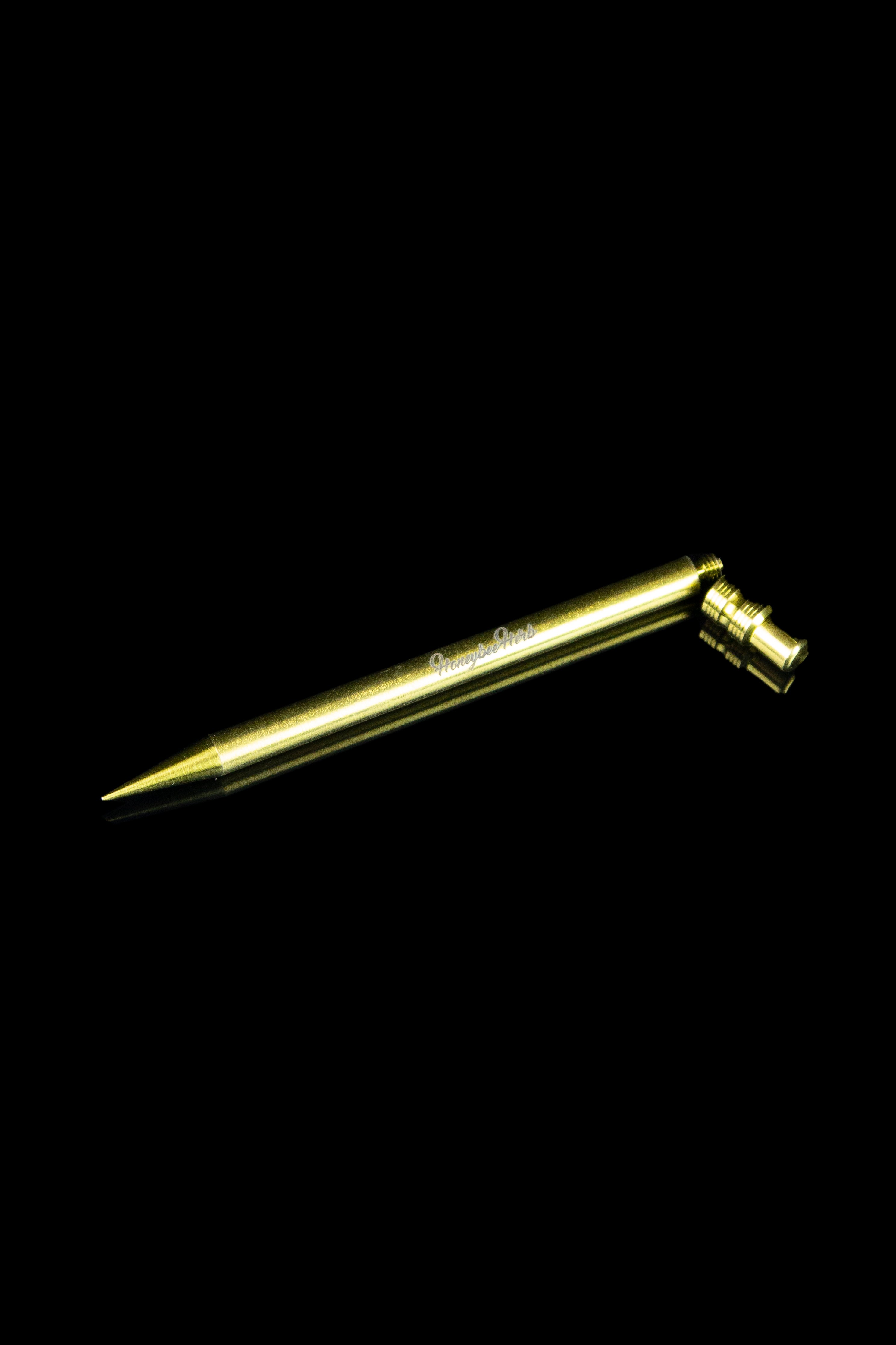 Gold-colored dab tool for cannabis concentrates against a black background.