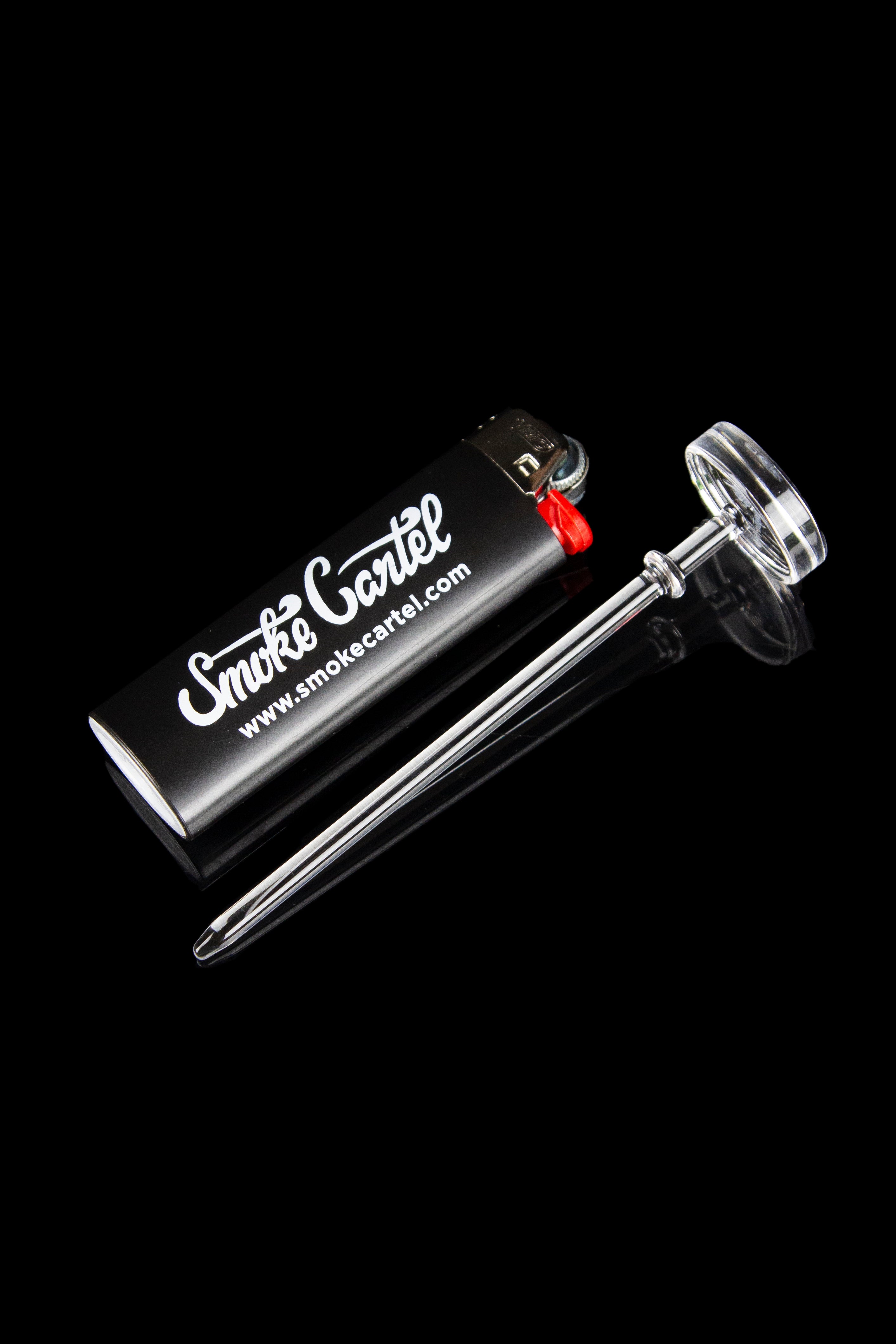 Glass dab tool and black lighter with "Smoke Cartel" logo on a dark background.