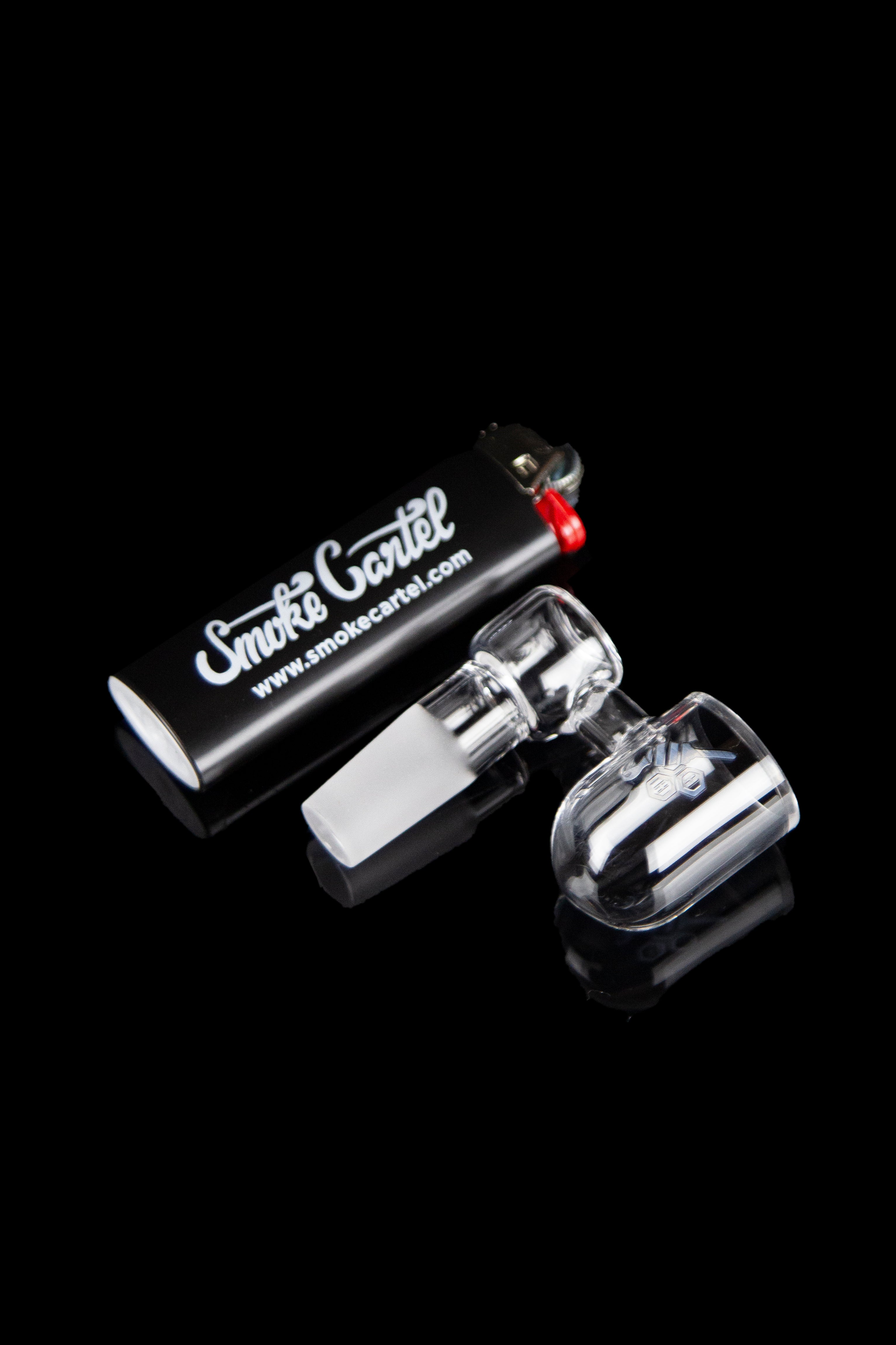 Clear glass dab rig with a carb cap and branded packaging on a black reflective surface.