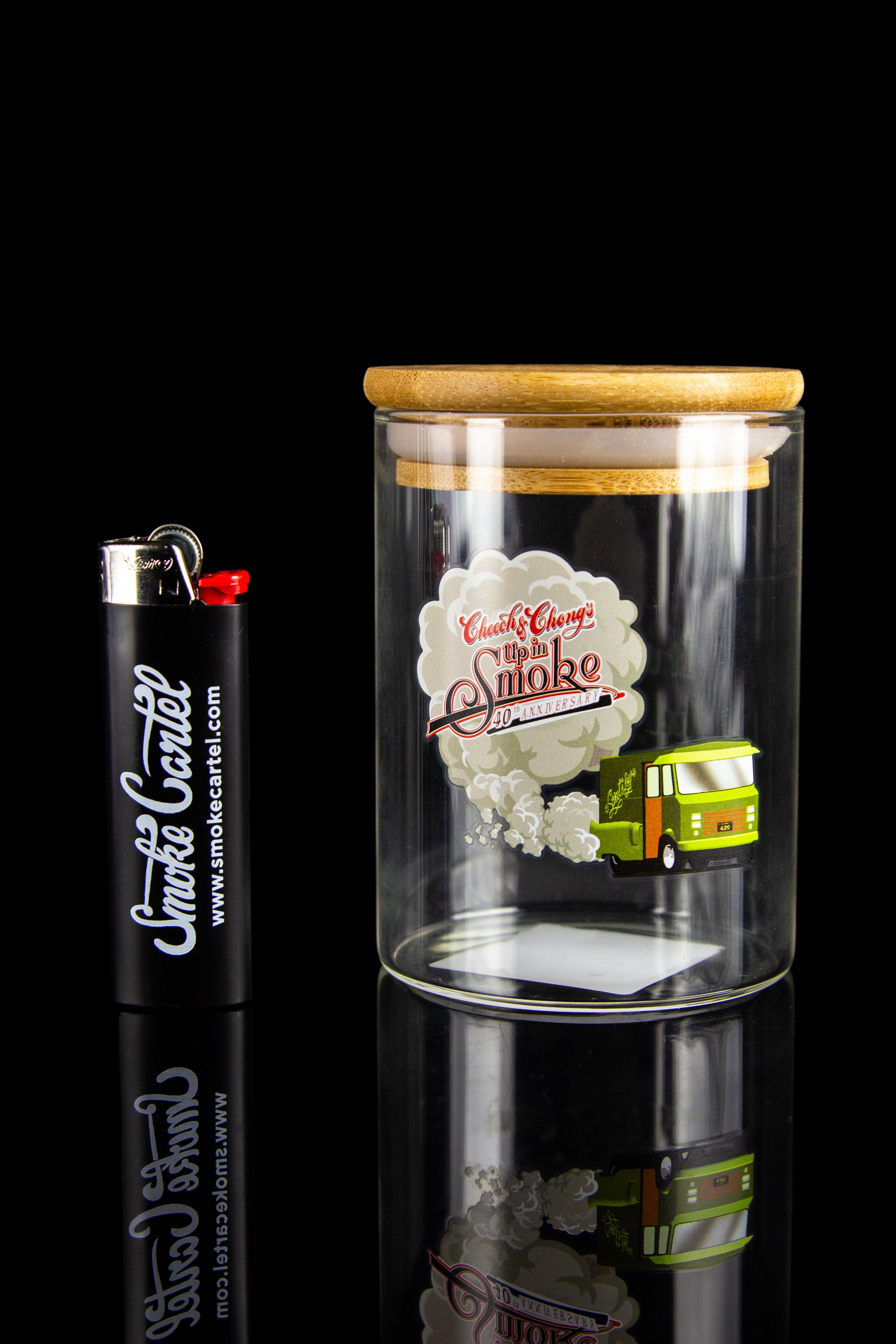 Glass storage jar with cannabis accessories, including a lighter and miniature van, displayed on a reflective black surface.