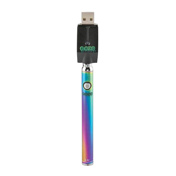 Centered, vertical front view of the rainbow-finish Ooze Slim Twist Battery with Charger plugged into the USB charger against a plain white background.