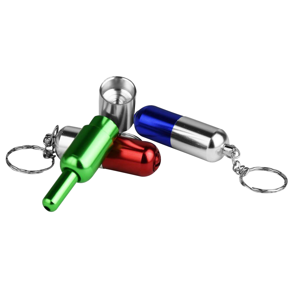 Angled close-up of three brightly anodized Pill Transformer Metal Hand Pipe keychain capsules in green, red and blue on a white background