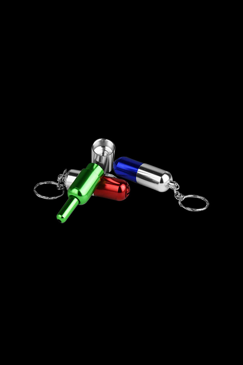 Close-up of three Pill Transformer Metal Hand Pipe keychain pieces in green, red and blue on a black background.