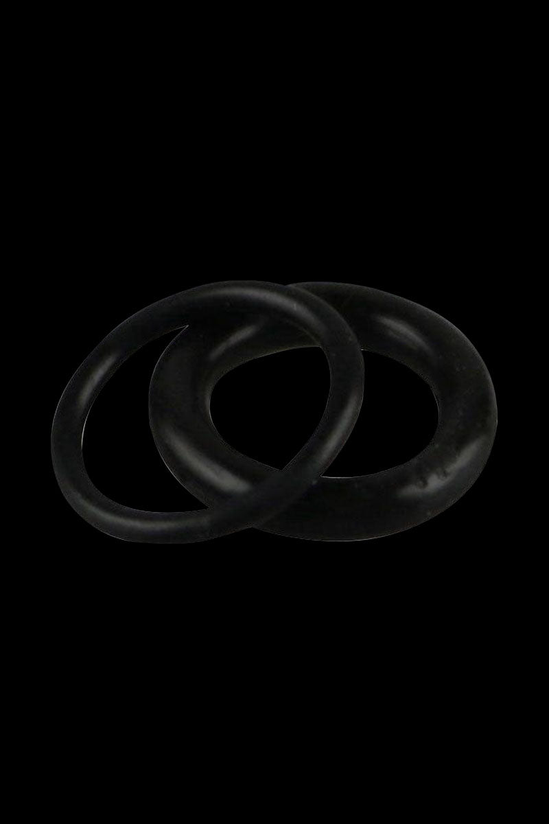 Close-up of two black Pulsar APX Wax/Barb Coil Replacement O-Rings - 2 Pack overlapped on a dark background, lit from above.