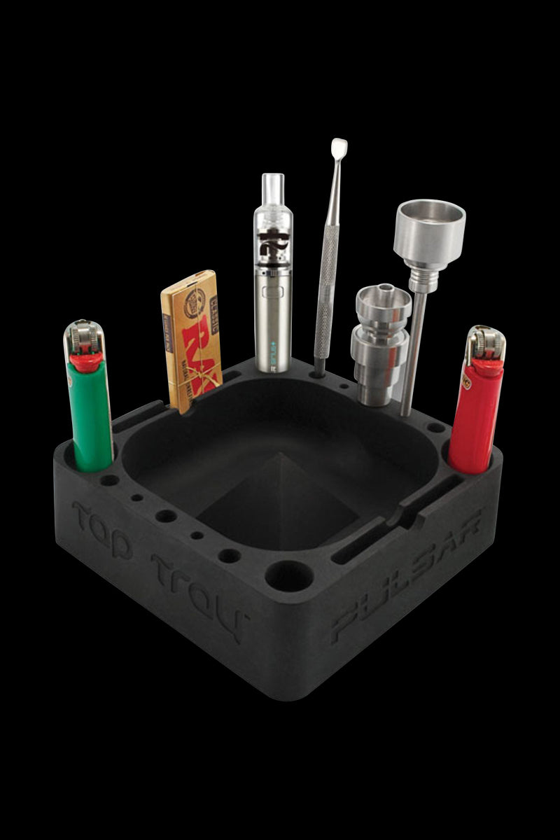Angled top-down view of a black Pulsar Tap Tray holding lighters, a small silver vaporizer, metal tools, and a pack of rolling papers against a black background