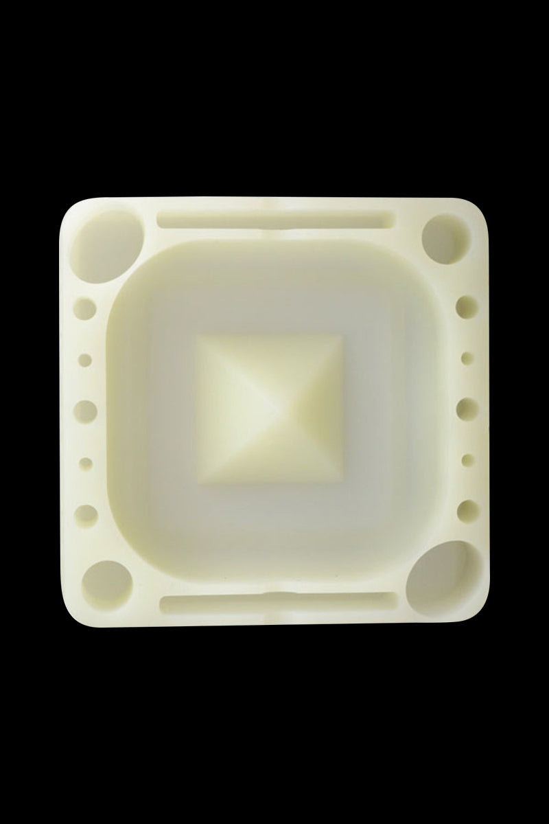 Top-down view of a cream-colored Pulsar Tap Tray showing its square recessed center with a raised pyramid and multiple circular and elongated compartments on a black background.