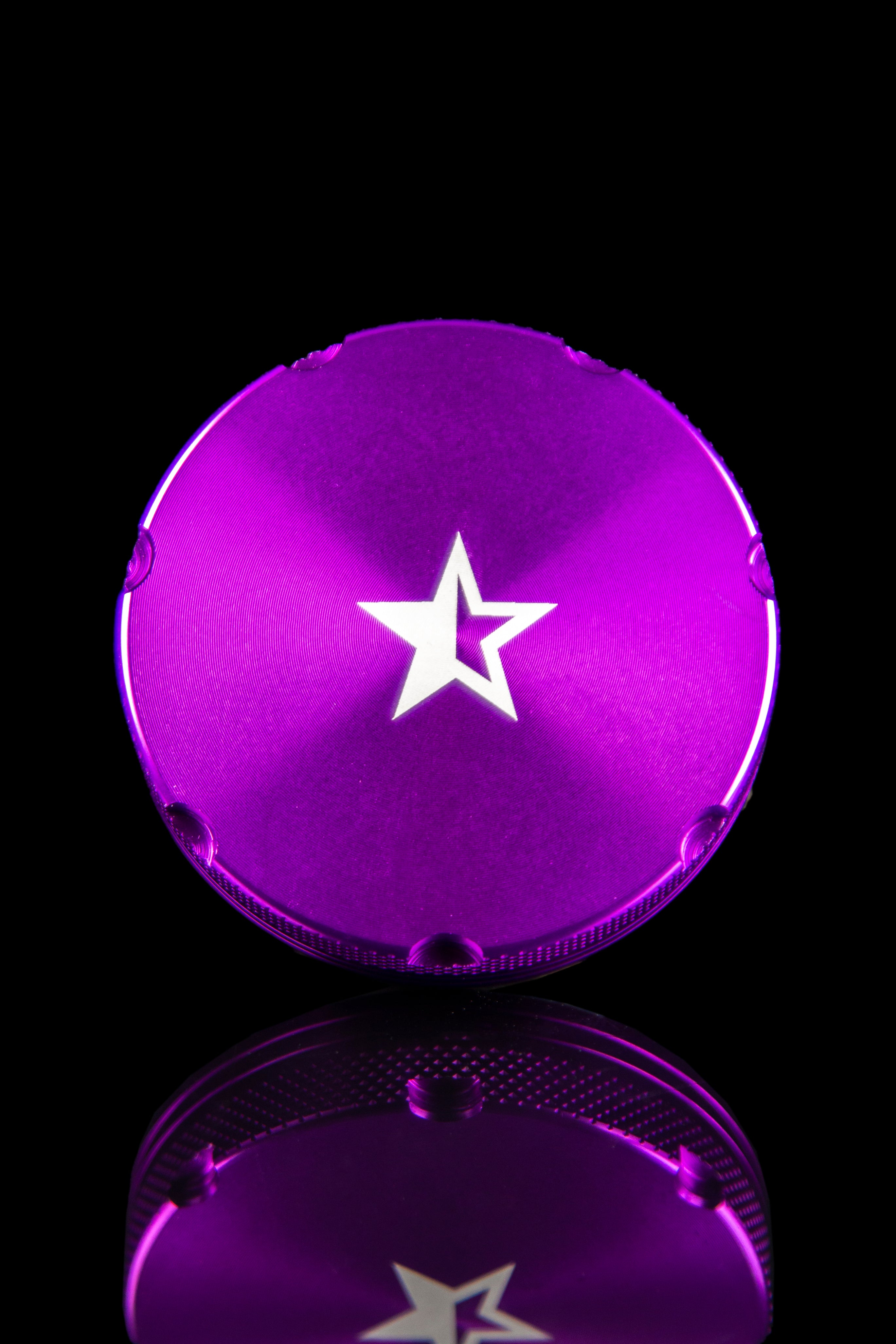 Close-up of the Famous X 4-Piece Grinder, with a dark background emphasizing its metallic finish and circular shape.