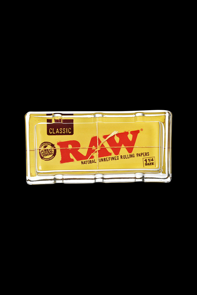 The RAW Classic Pack Glass Ashtray is shown in a close-up, angled view with visible branding on a black background.