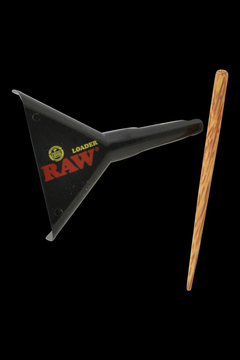 Angled top-down view of a black RAW Cone Loader for Lean & 1 1/4" Cones beside a wood-textured packing stick on a black background