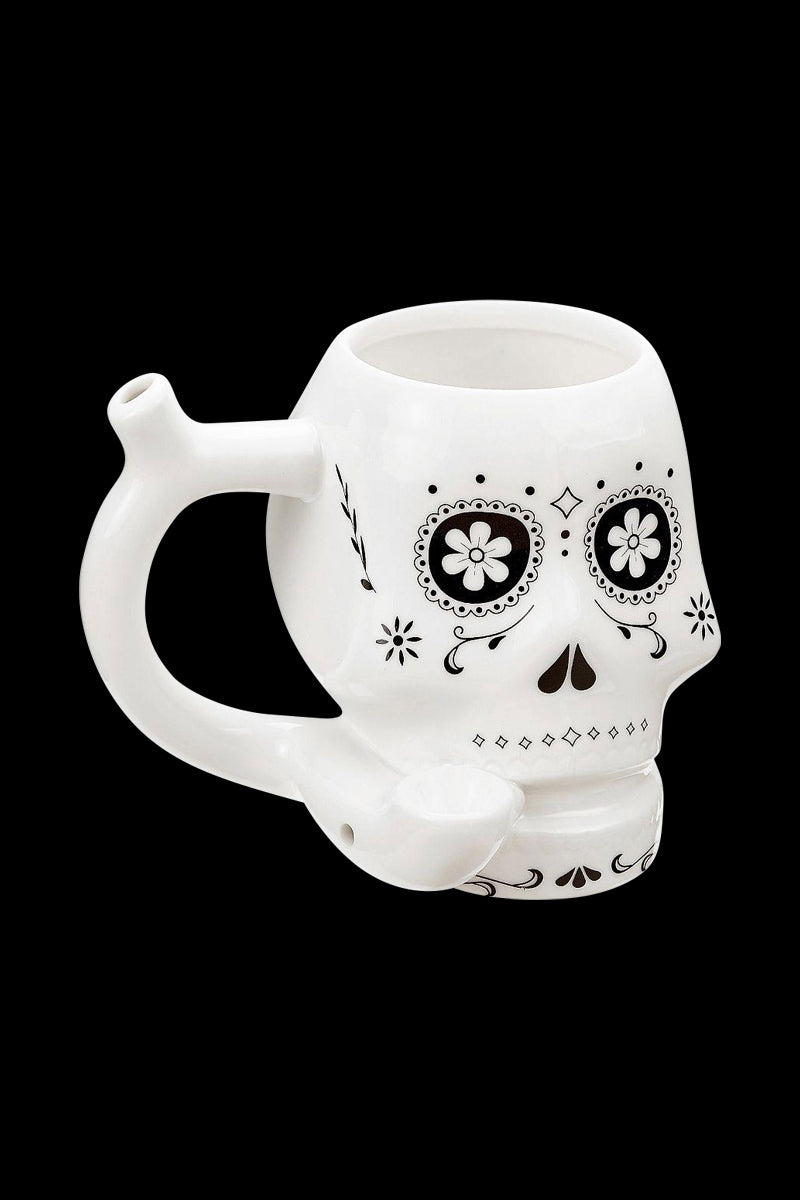 Three-quarter view of the Roast & Toast "Sugar Skull" Ceramic Pipe Mug showing the white skull-shaped mug with black floral eye designs and a curved pipe handle against a black background