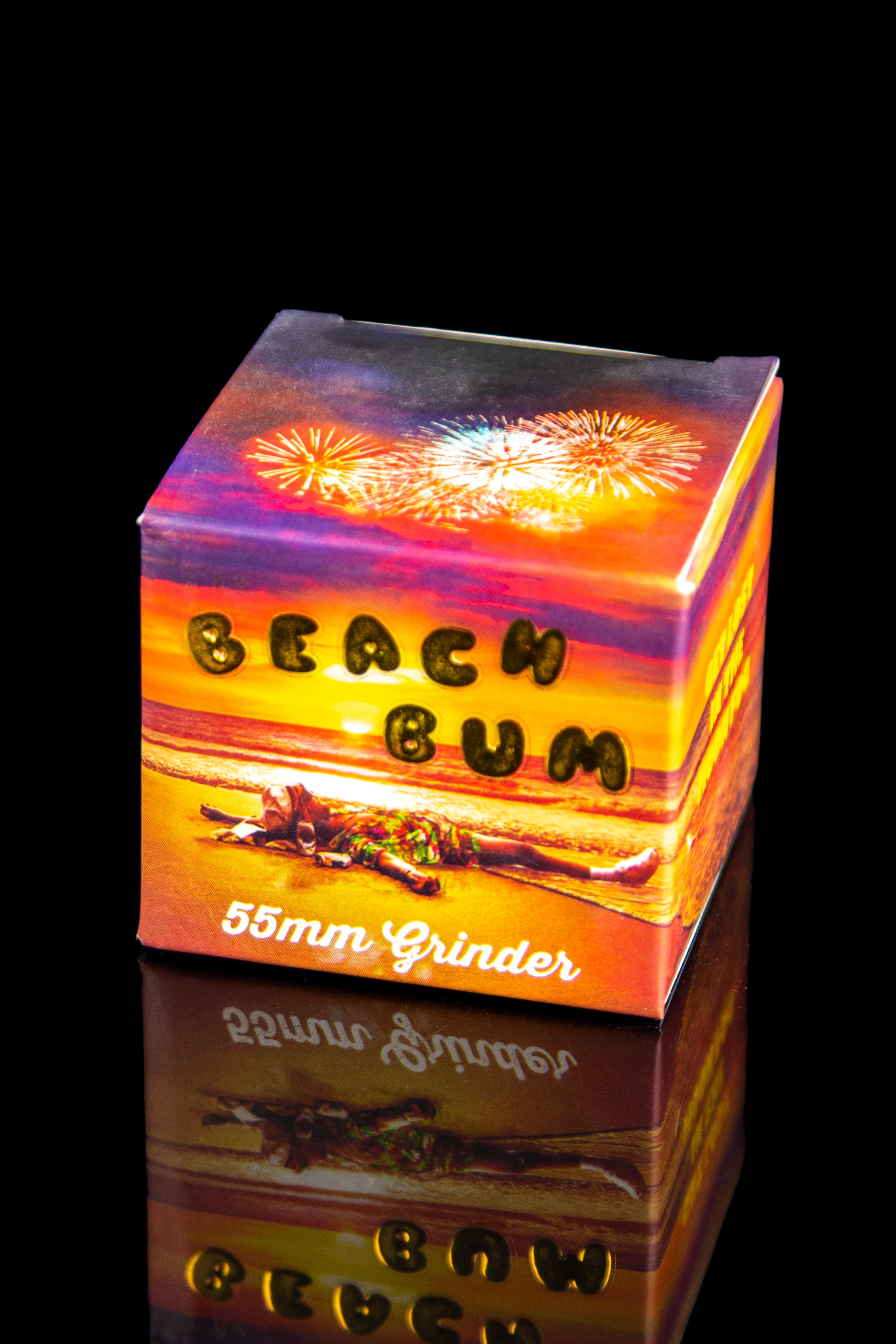 Box for a "Beach Bum" 55mm grinder with a sunset and palm tree design, reflecting on a dark surface.