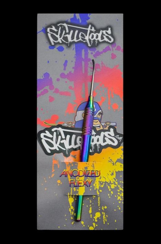 Top-down view of a rainbow anodized Skilletools Anodized Series Dab Tools "Scoop Dog" placed upright on colorful graffiti-style packaging with purple, orange, and yellow paint splatters.