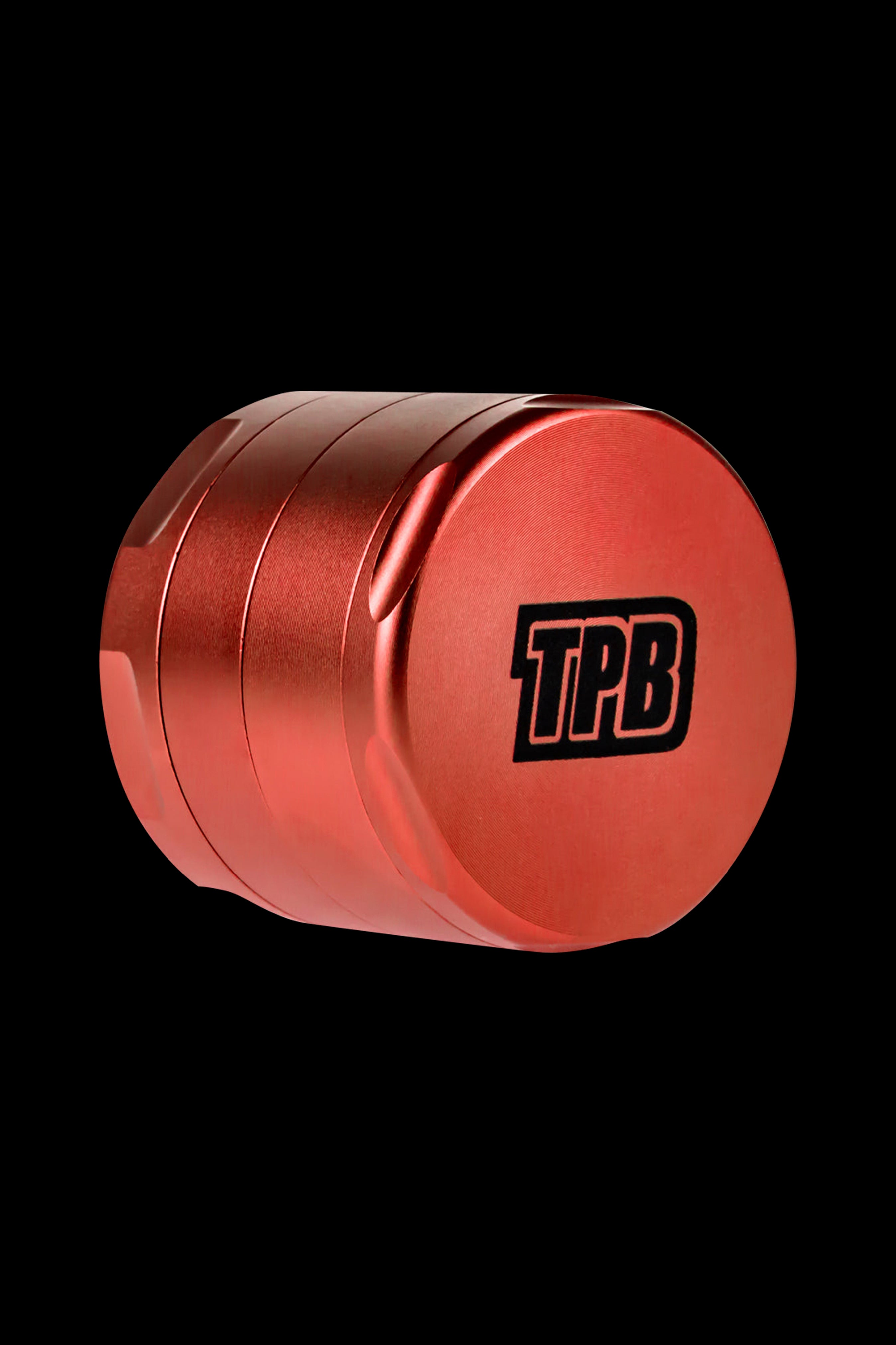 Red metal cannabis grinder with "TPB" logo against a black background.