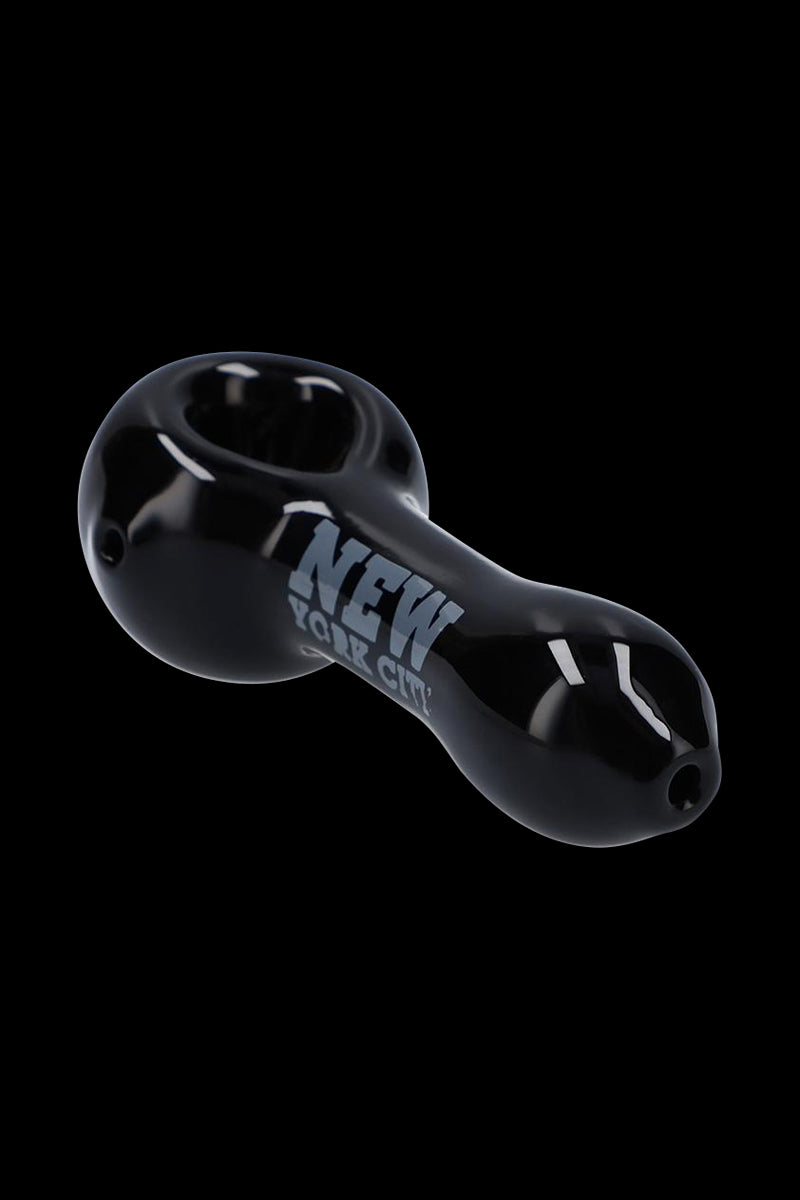 Angled close-up of the black Rock Legends Glass Spoon Pipe - Jimi NYC against a solid black background showing glossy reflections and "NEW YORK CITY" text.