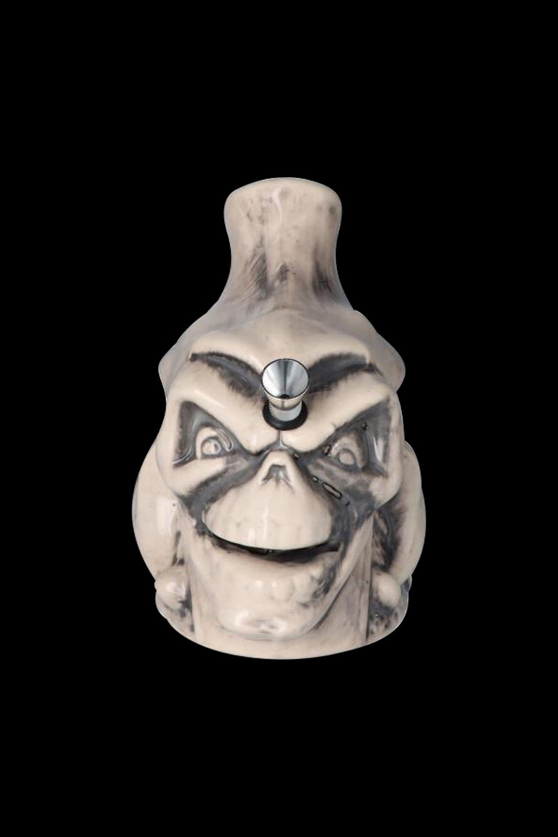 Front-facing view of the Smiling Skull Ceramic Pipe showing a pale, grinning skull face with dark shaded features and a metal bowl at the forehead.