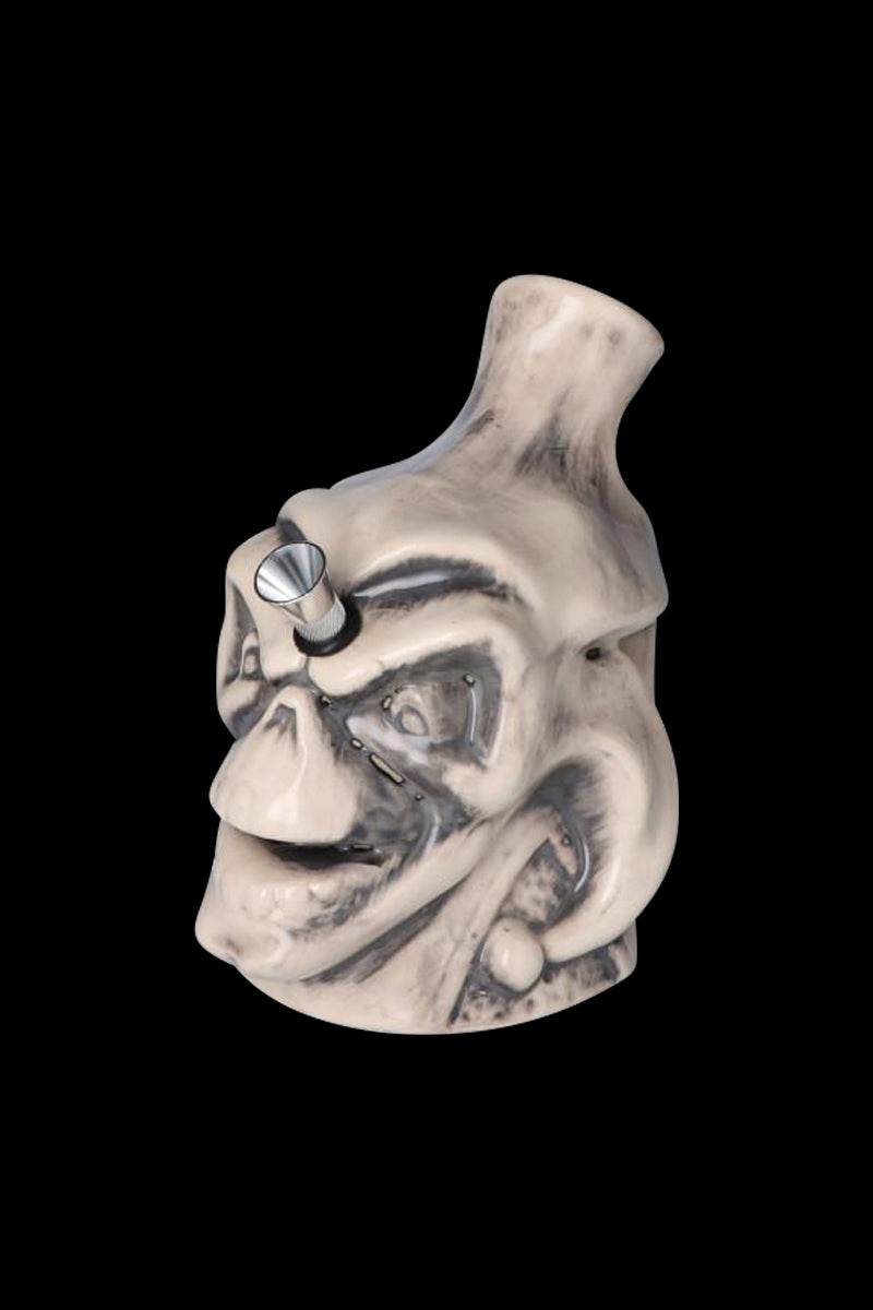 Three-quarter view of the Smiling Skull Ceramic Pipe showing its pale, weathered skull face and metal bowl against a black background