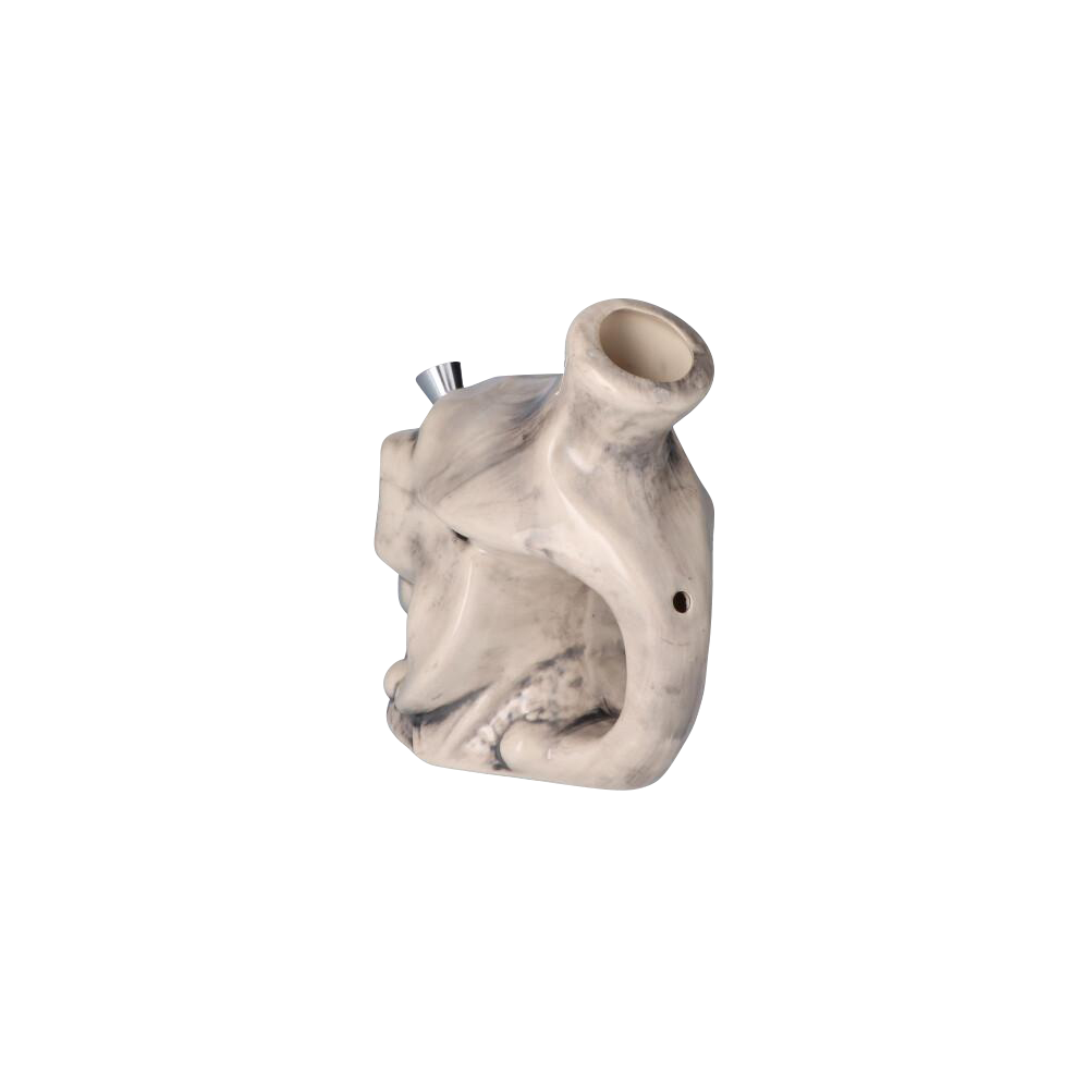 Angled three-quarter view of the Smiling Skull Ceramic Pipe showing its creamy marbled ceramic skull shape with a metal bowl and top-lit opening.