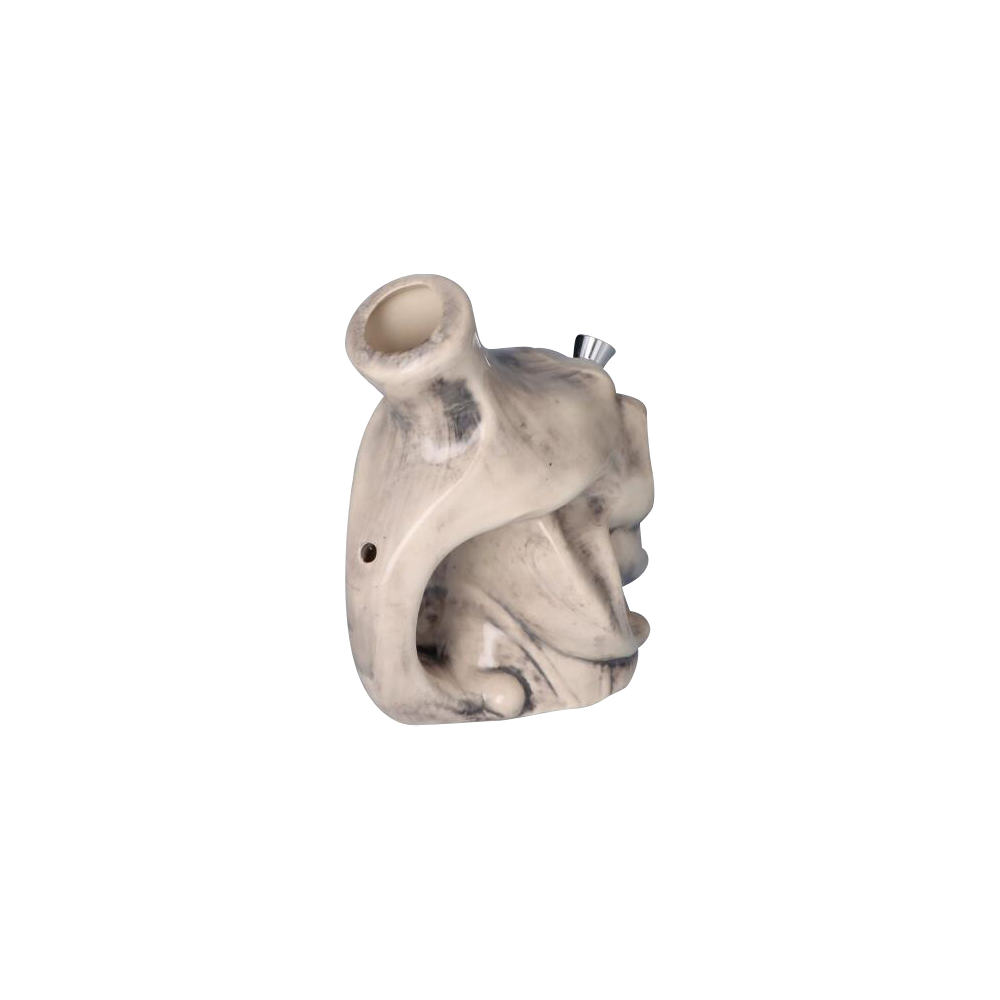 Angled close-up of the Smiling Skull Ceramic Pipe showing its white marbled ceramic surface, rounded bowl and carved hollow form.