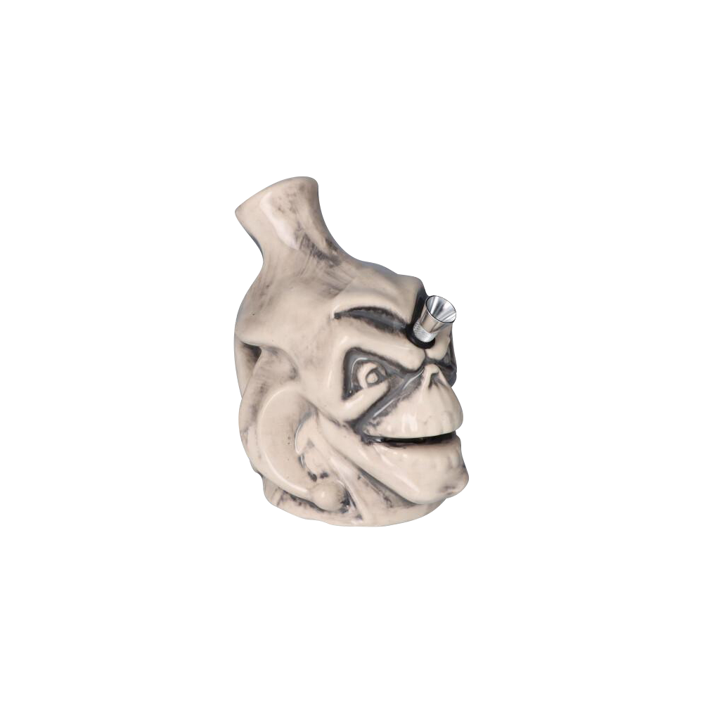 Front three-quarter view of the Smiling Skull Ceramic Pipe showing its cream-glazed skull face with darkened creases and a metal bowl angled from the forehead