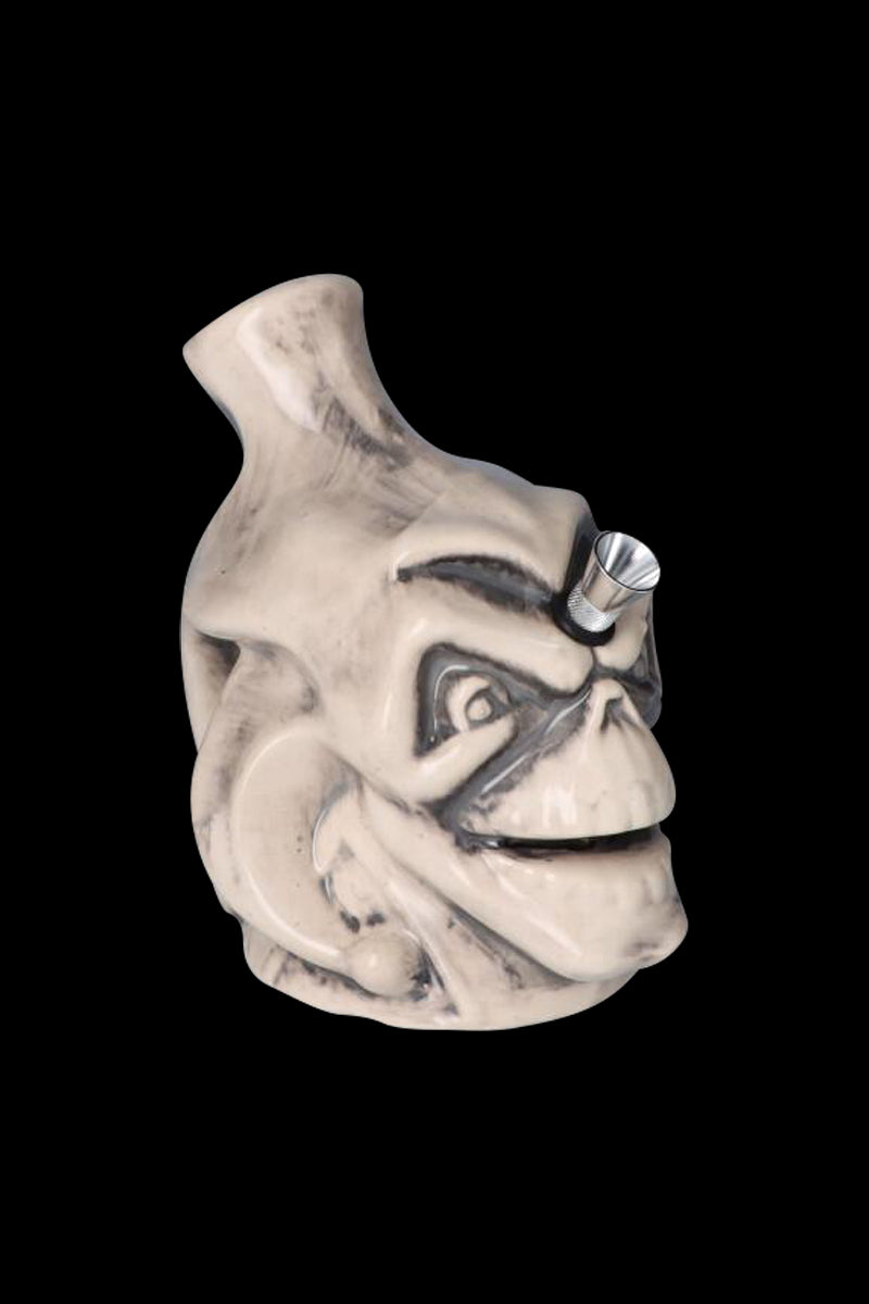 Three-quarter view of the Smiling Skull Ceramic Pipe in off-white ceramic with dark wash showing carved eye sockets and a metal bowl on the nose