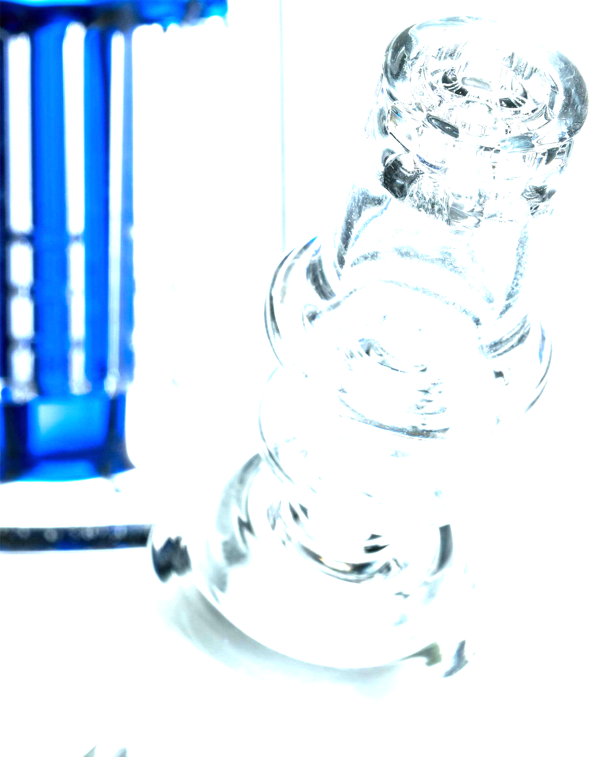 Angled close-up of a clear glass spiral joint on a Diamond Knot Domeless Nail against a black background with a blurred blue component at left