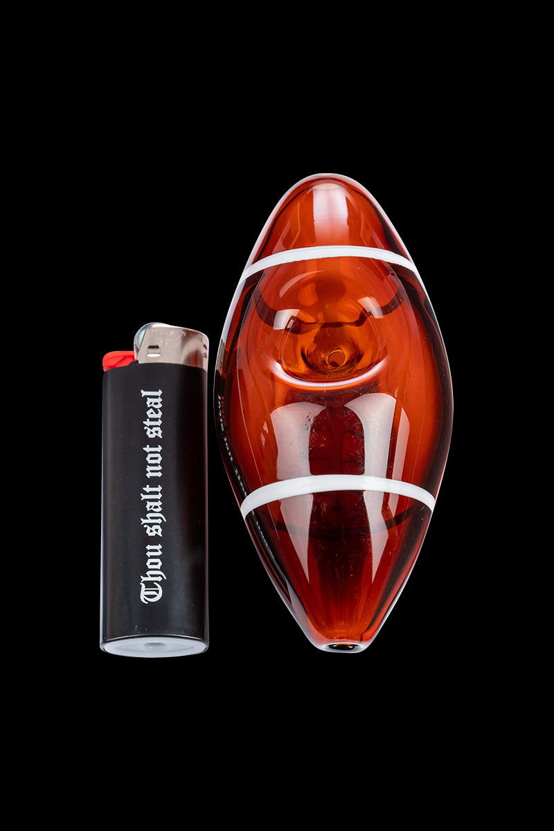 Top-down view of a translucent amber Football Hand Pipe with white stripes shown beside a black lighter.