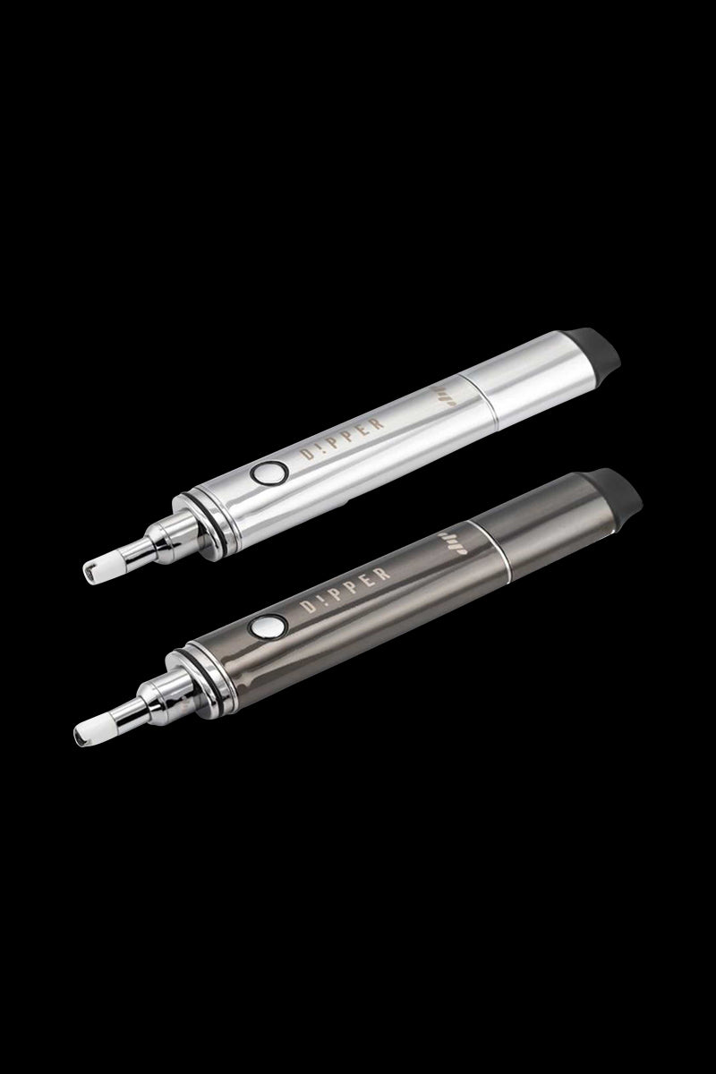 Angled top-down view of two metallic Dip Devices Vaporizer - The Dipper pens, one silver and one gunmetal, on a black background.